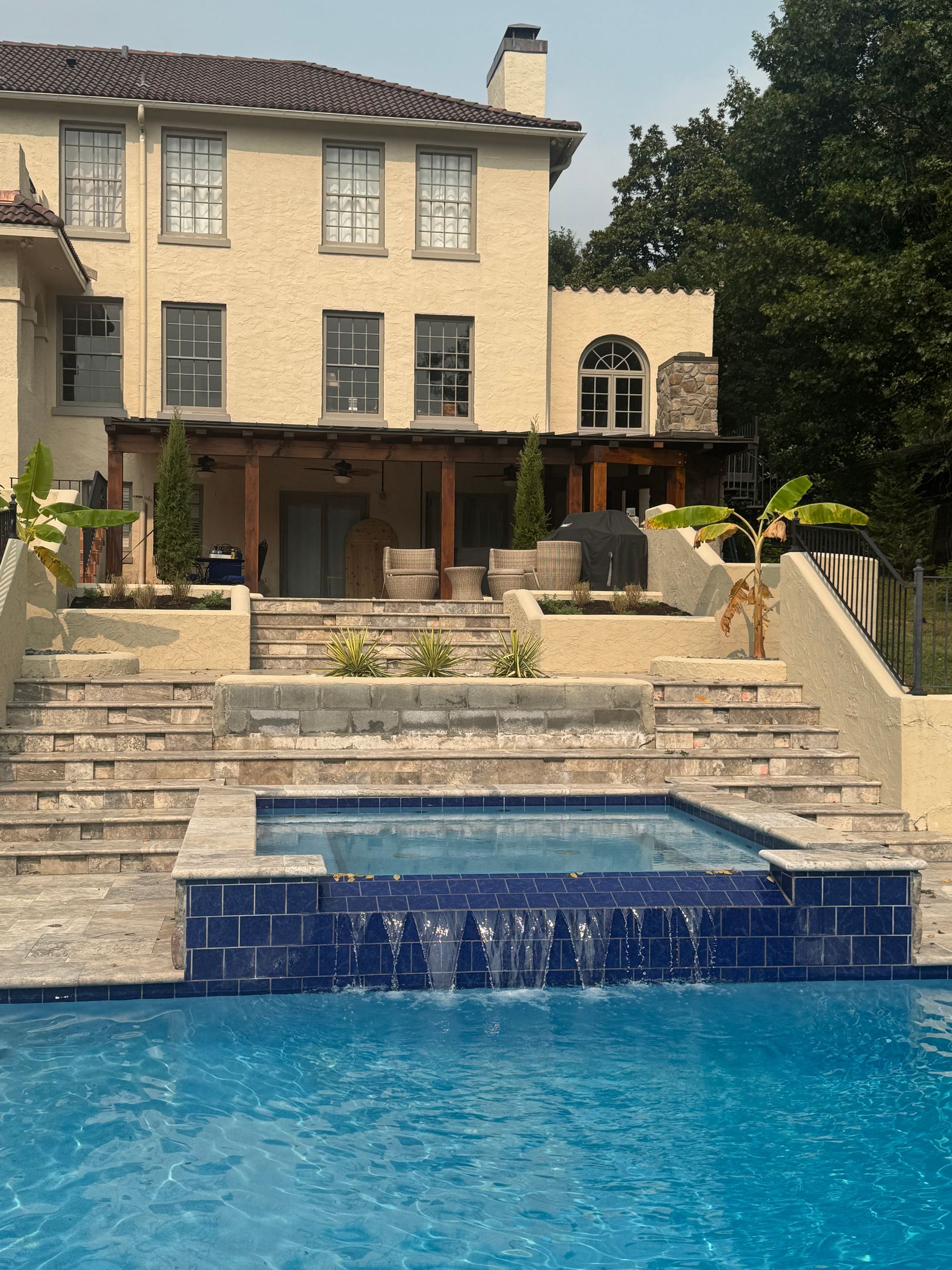 Stone mansion with tiered patio and blue swimming pool in the foreground