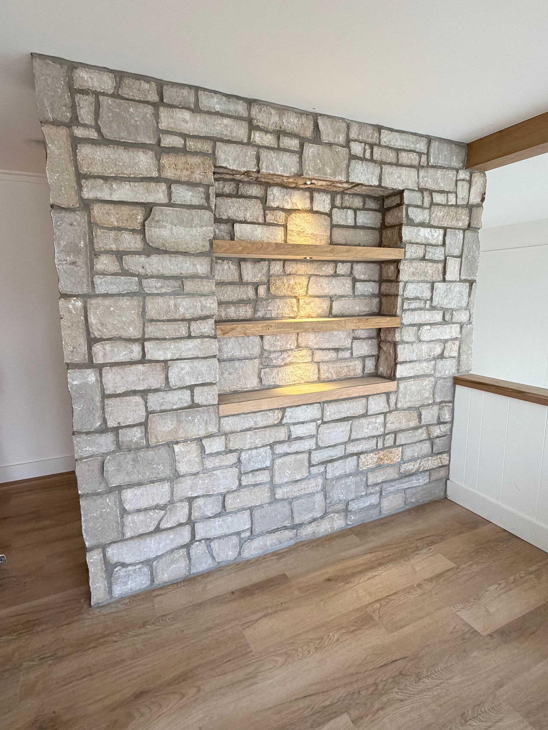 Stone accent wall with built-in shelves in a modern room with wood flooring