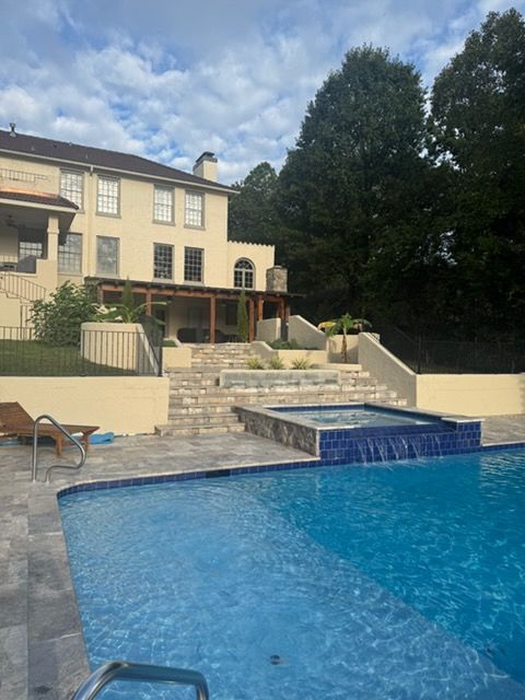 Outdoor pool with blue water in front of a beige house and stone patio under a cloudy sky