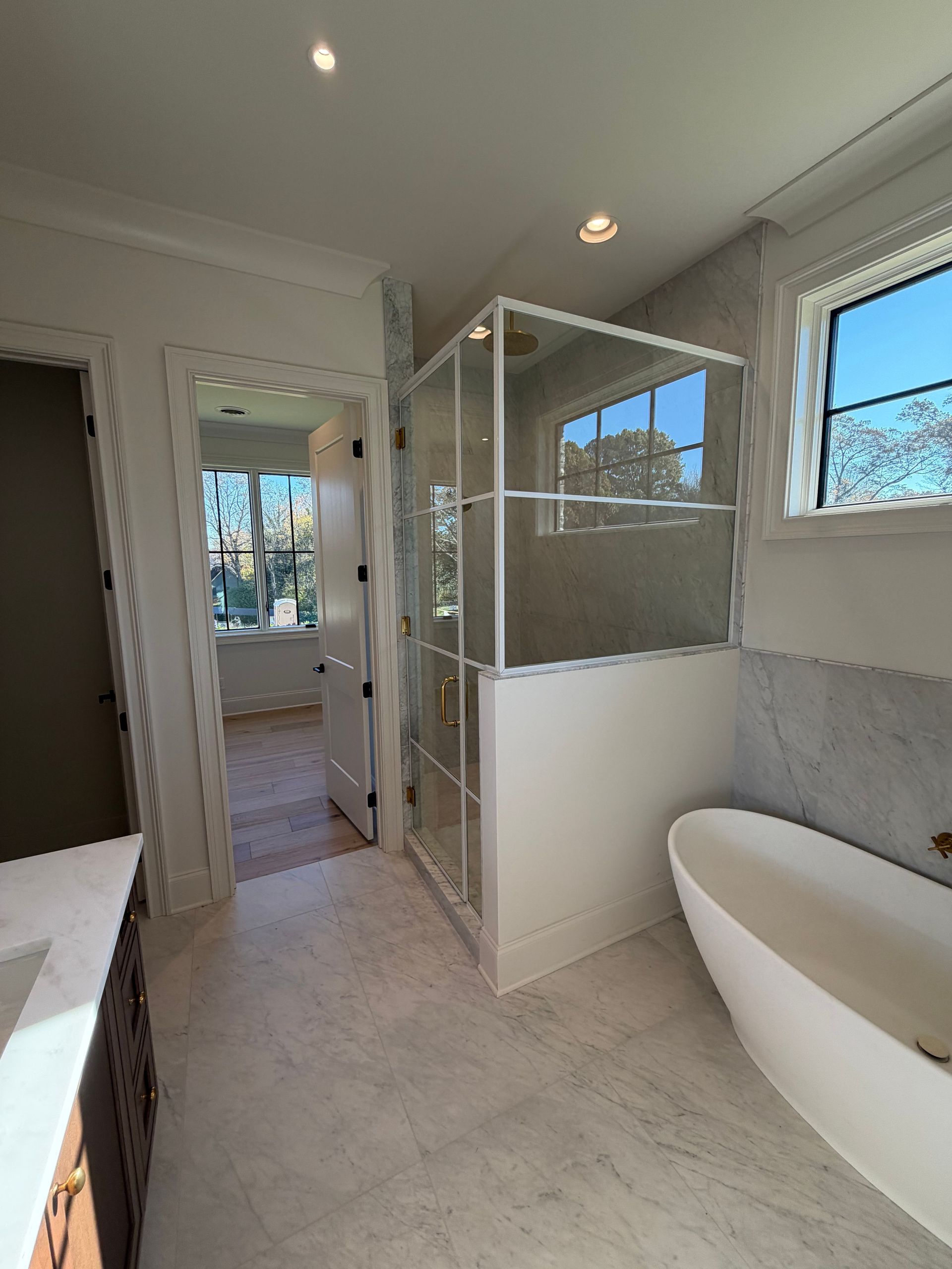 Bright bathroom with tiled floor, glass shower enclosure, and white bathtub by a window.