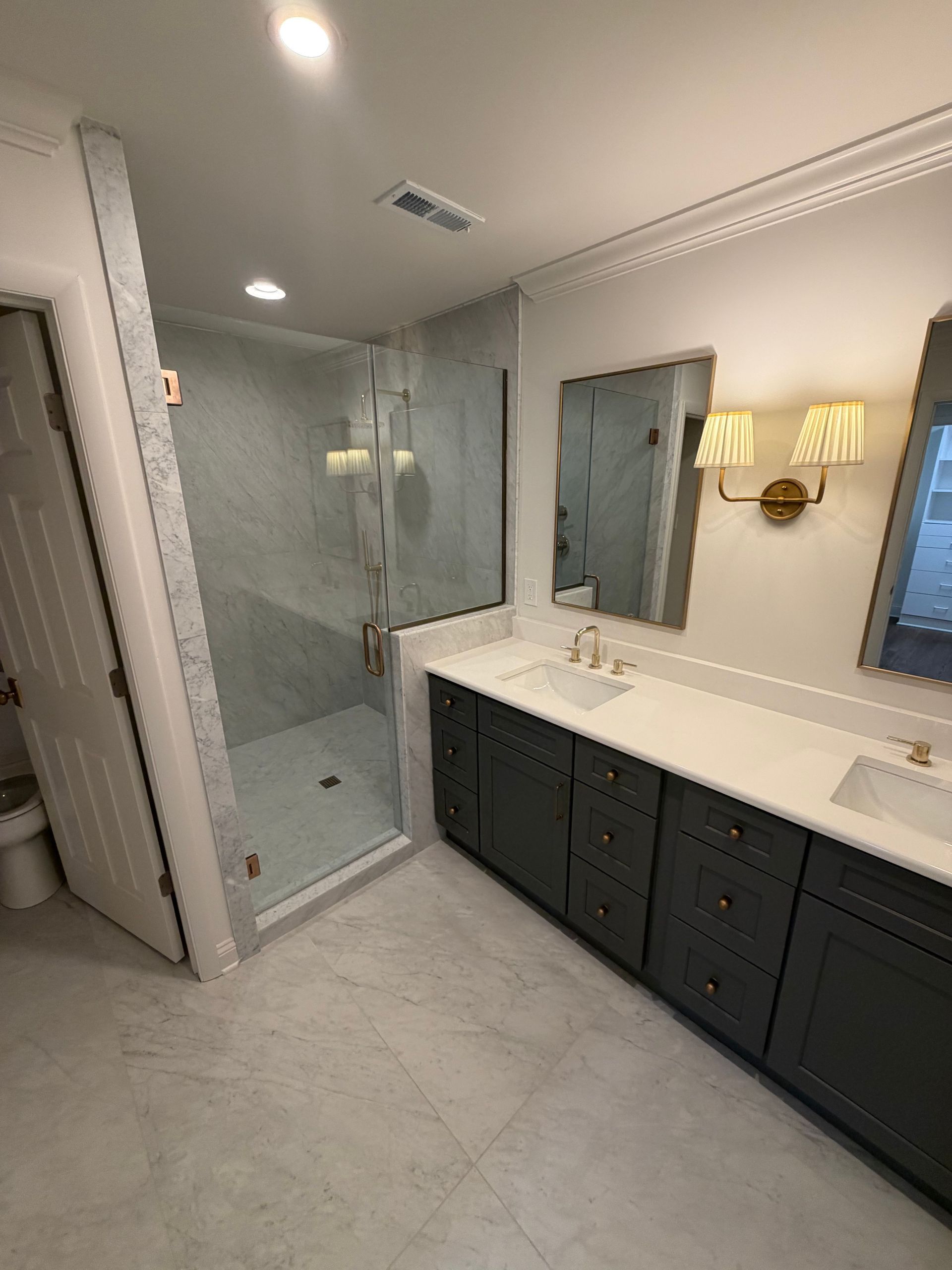 Modern bathroom with glass shower, double vanity, mirror, and dark cabinet doors