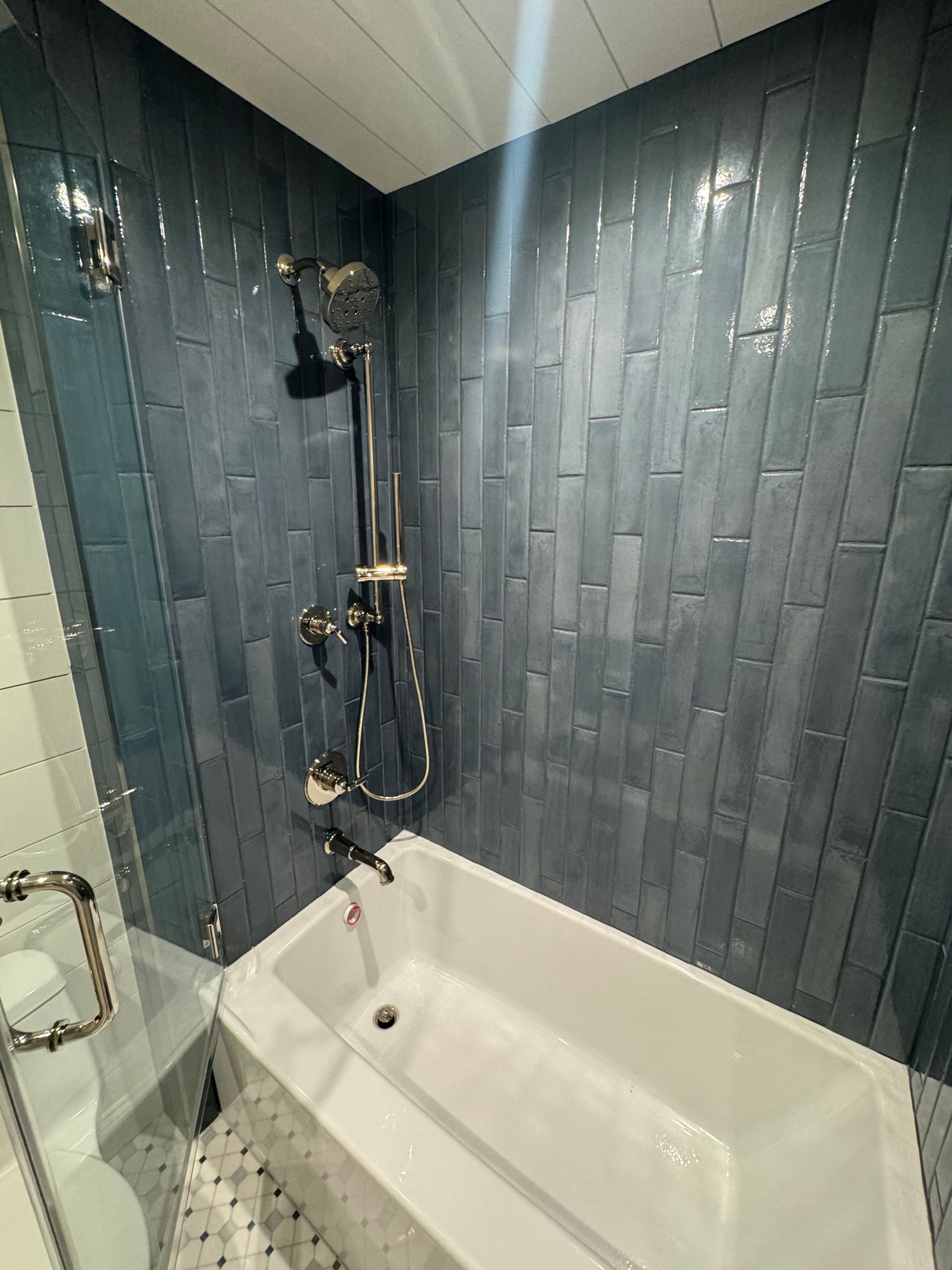 Bathroom shower and bathtub with dark blue tile walls and chrome fixtures