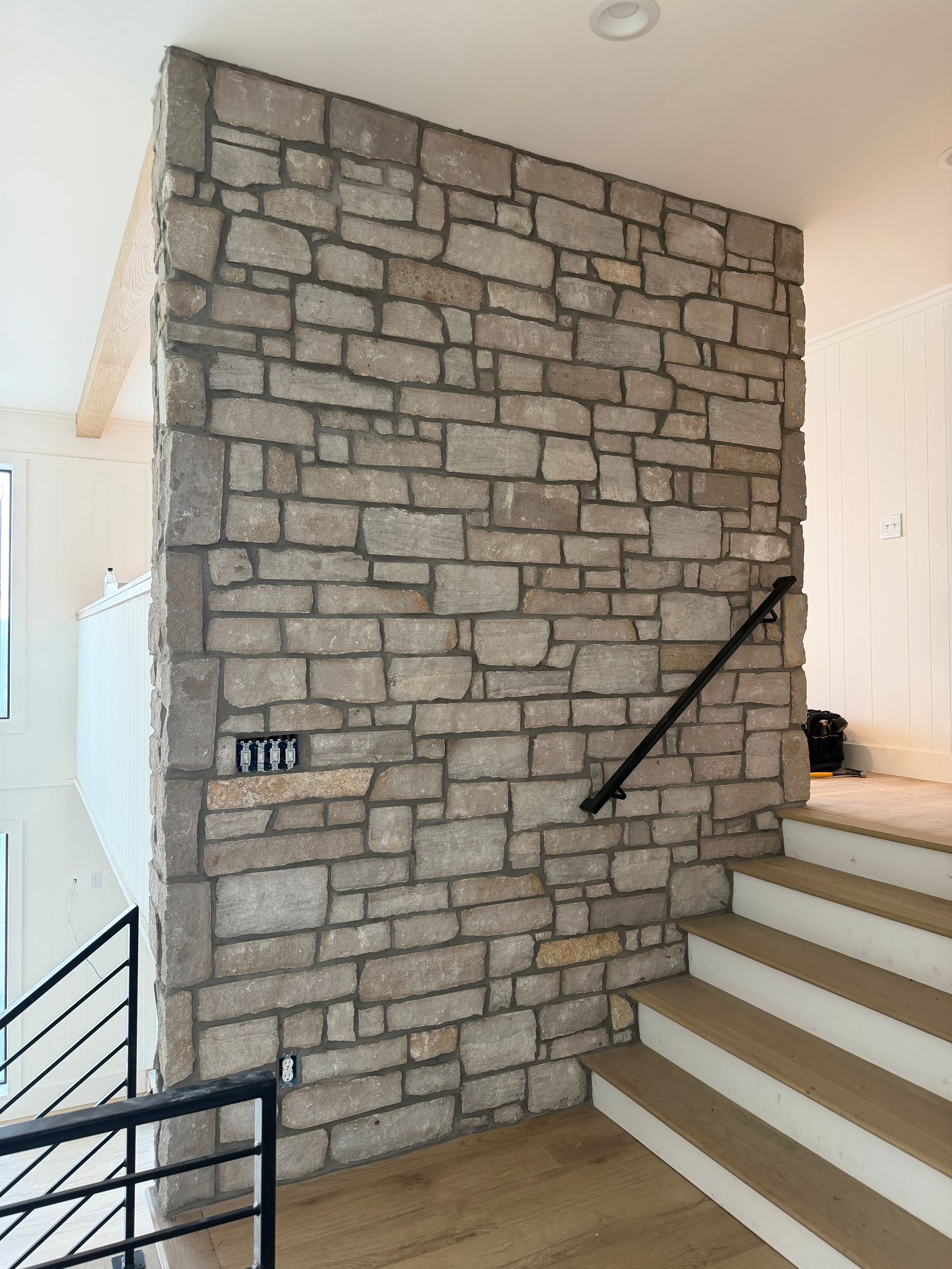 Stone accent wall beside a staircase with black handrail in a bright interior hallway