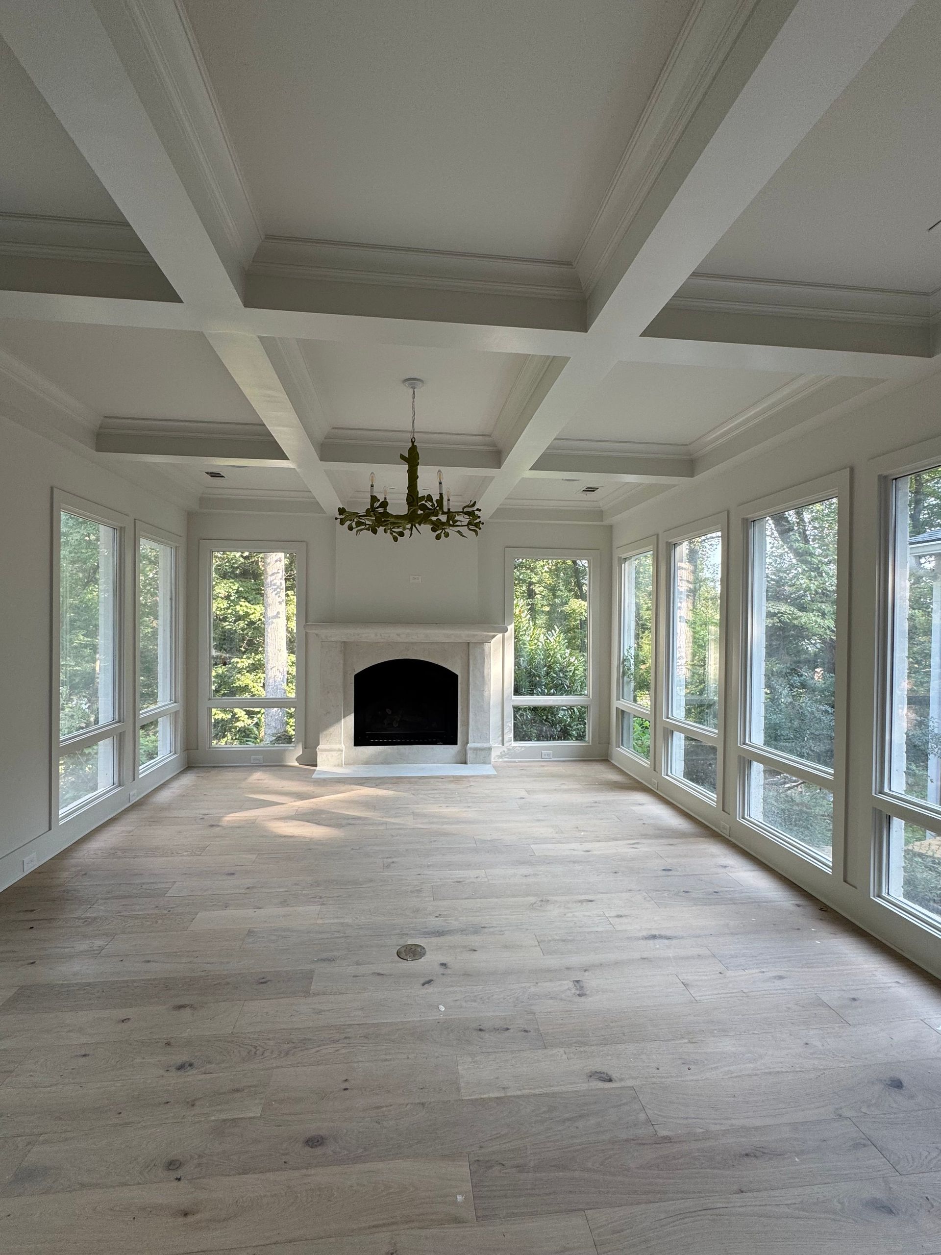 Empty sunroom with white beams, chandelier, large windows, and a fireplace on the far wall.