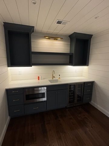 Modern dark kitchen with white shiplap walls, black cabinets, and stainless sink and oven.