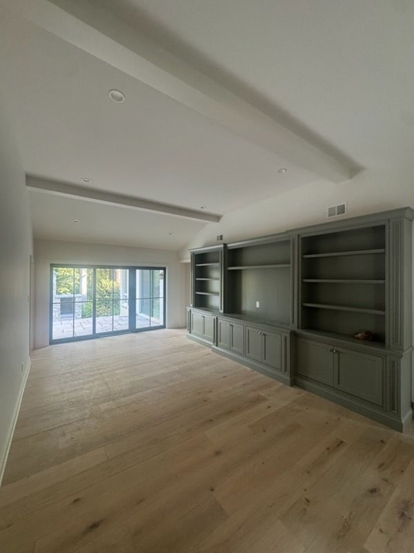 Empty modern living room with built-in green cabinets, light wood floors, and large sliding glass doors