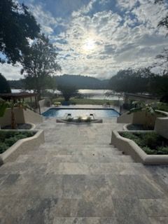 Stone steps lead to a pool and lake at sunset, framed by trees and a cloudy sky.