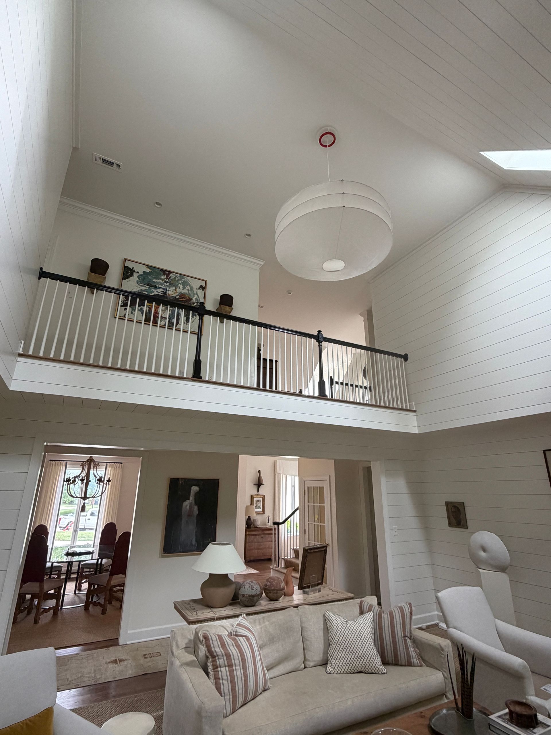 Two-story living room with balcony, white walls, and large chandelier above a sofa and staircase.