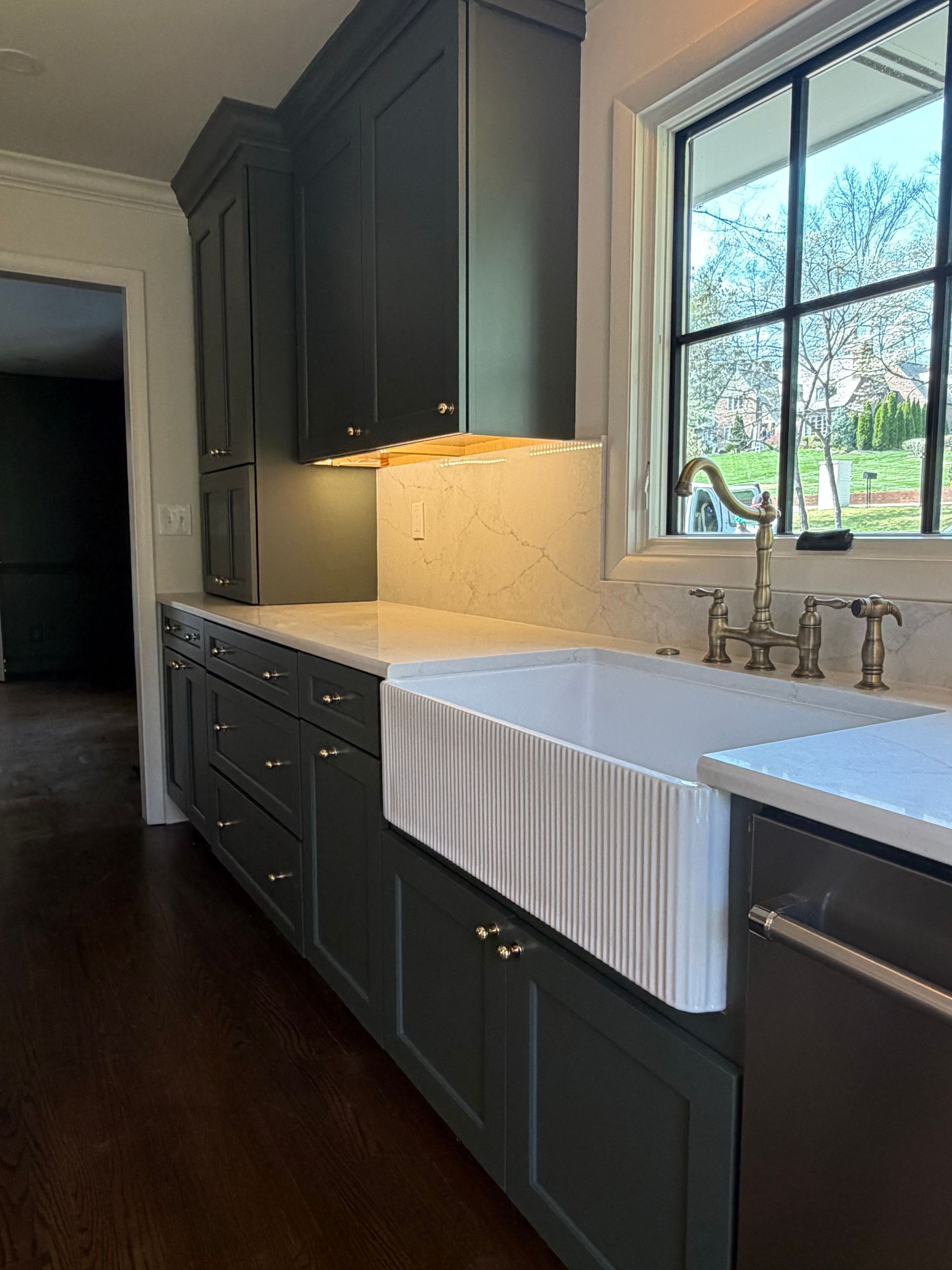 Modern kitchen with dark cabinets, white farmhouse sink, and sunlit window above the counter