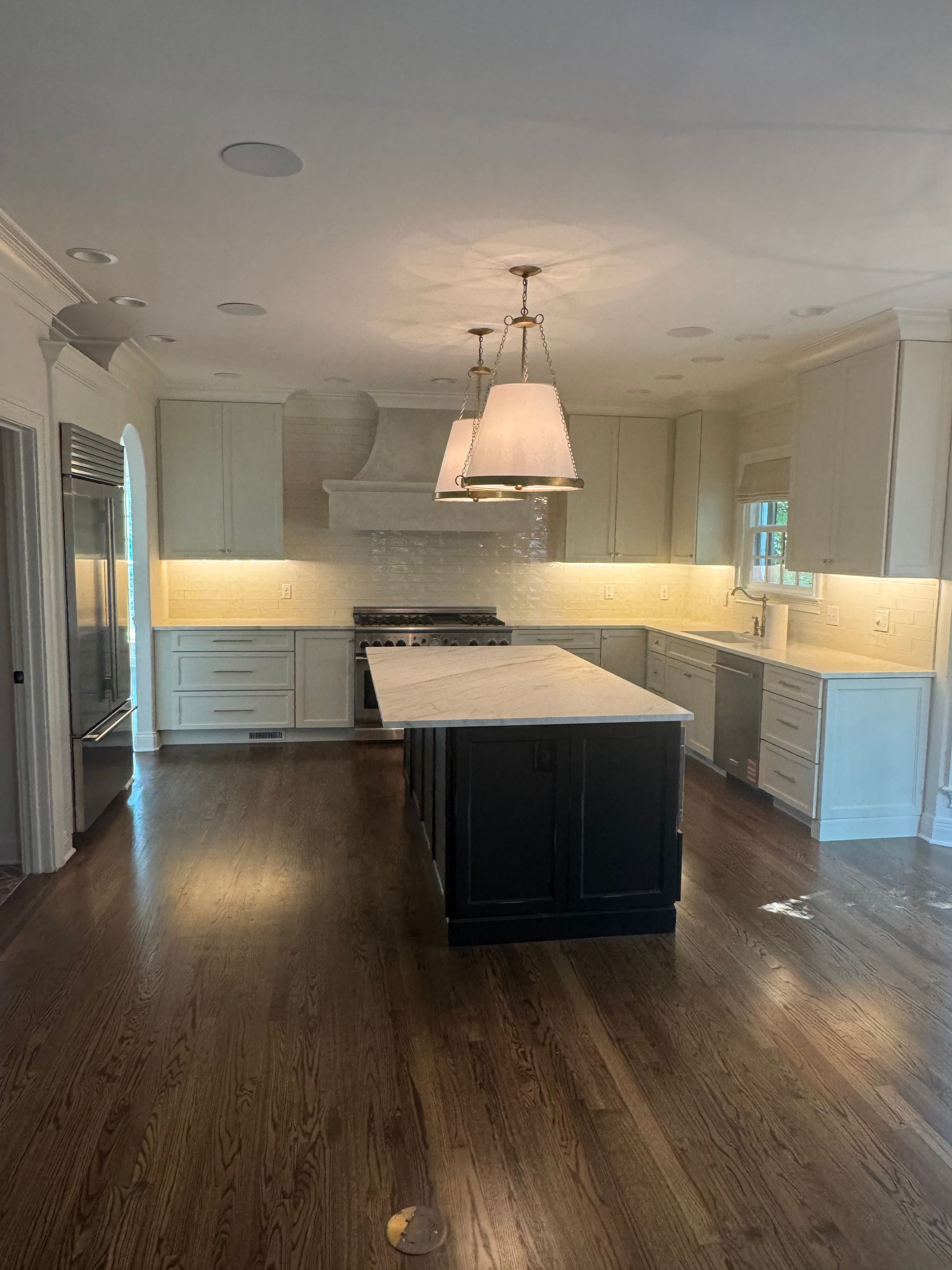 Bright modern kitchen with white cabinets, dark wood floors, and a large island centered under pendant lights