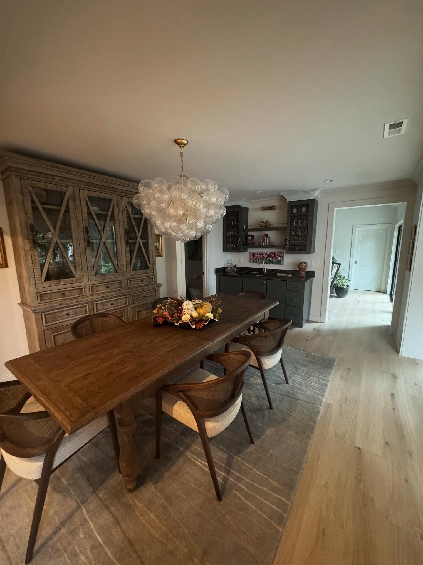 Modern dining room with wooden table, upholstered chairs, crystal chandelier, and fireplace in the background