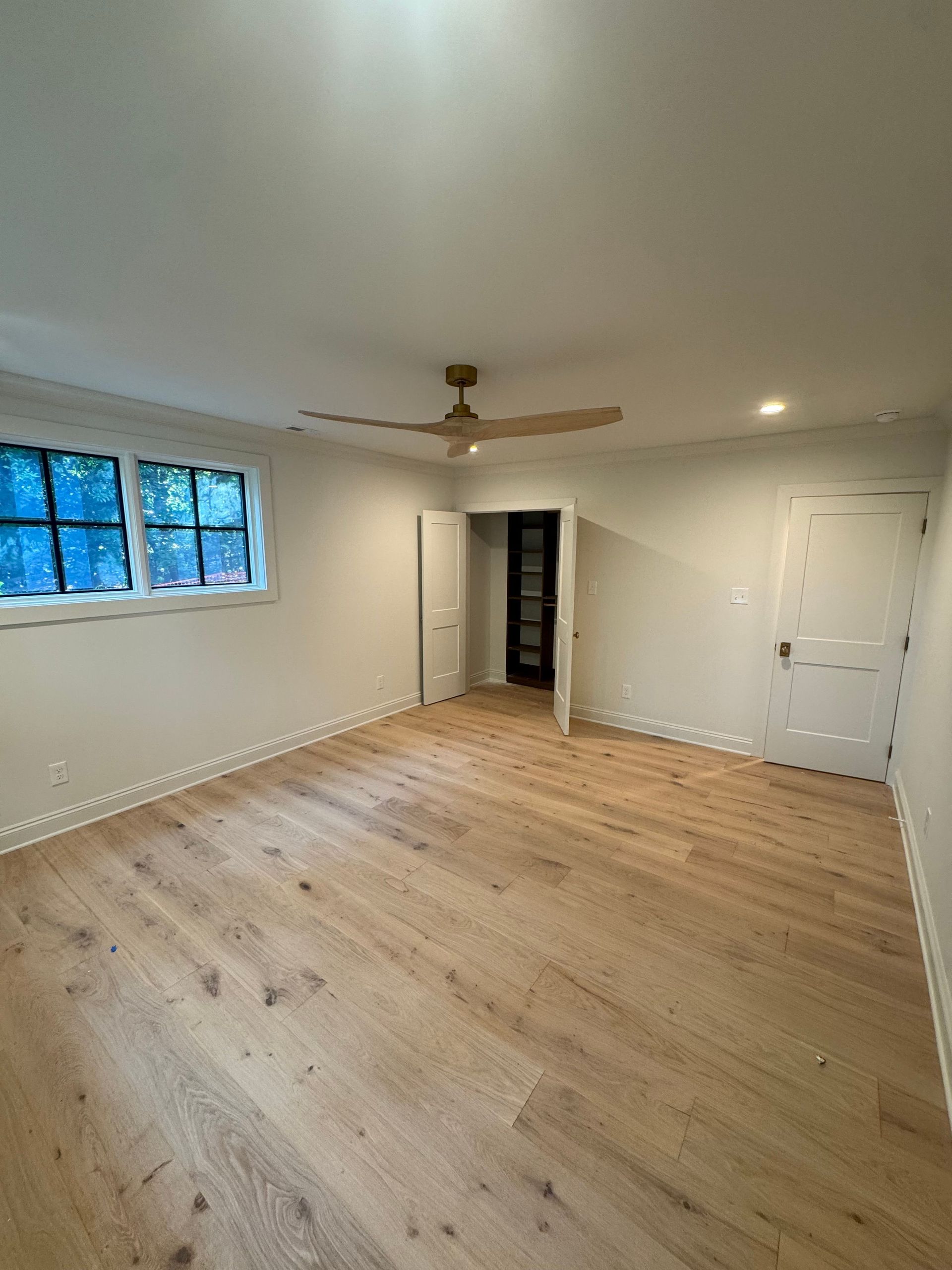 Empty room with light wood floors, white walls, ceiling fan, window, closet, and recessed lights.