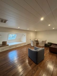Bright living room with wood floors, white walls, projector screen, and gray and brown chairs