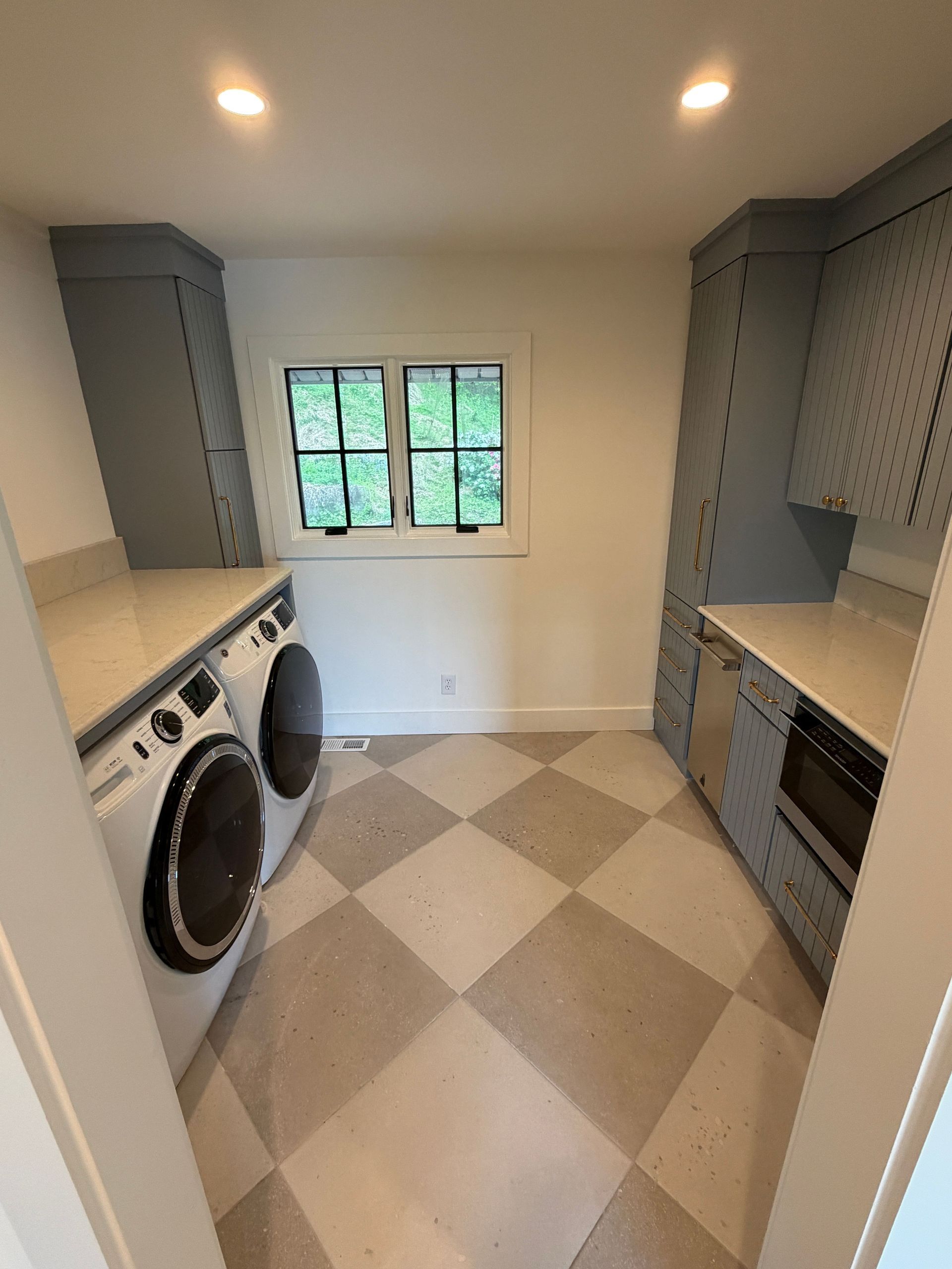 Narrow laundry room with washer, dryer, built-in cabinets, and a small window.