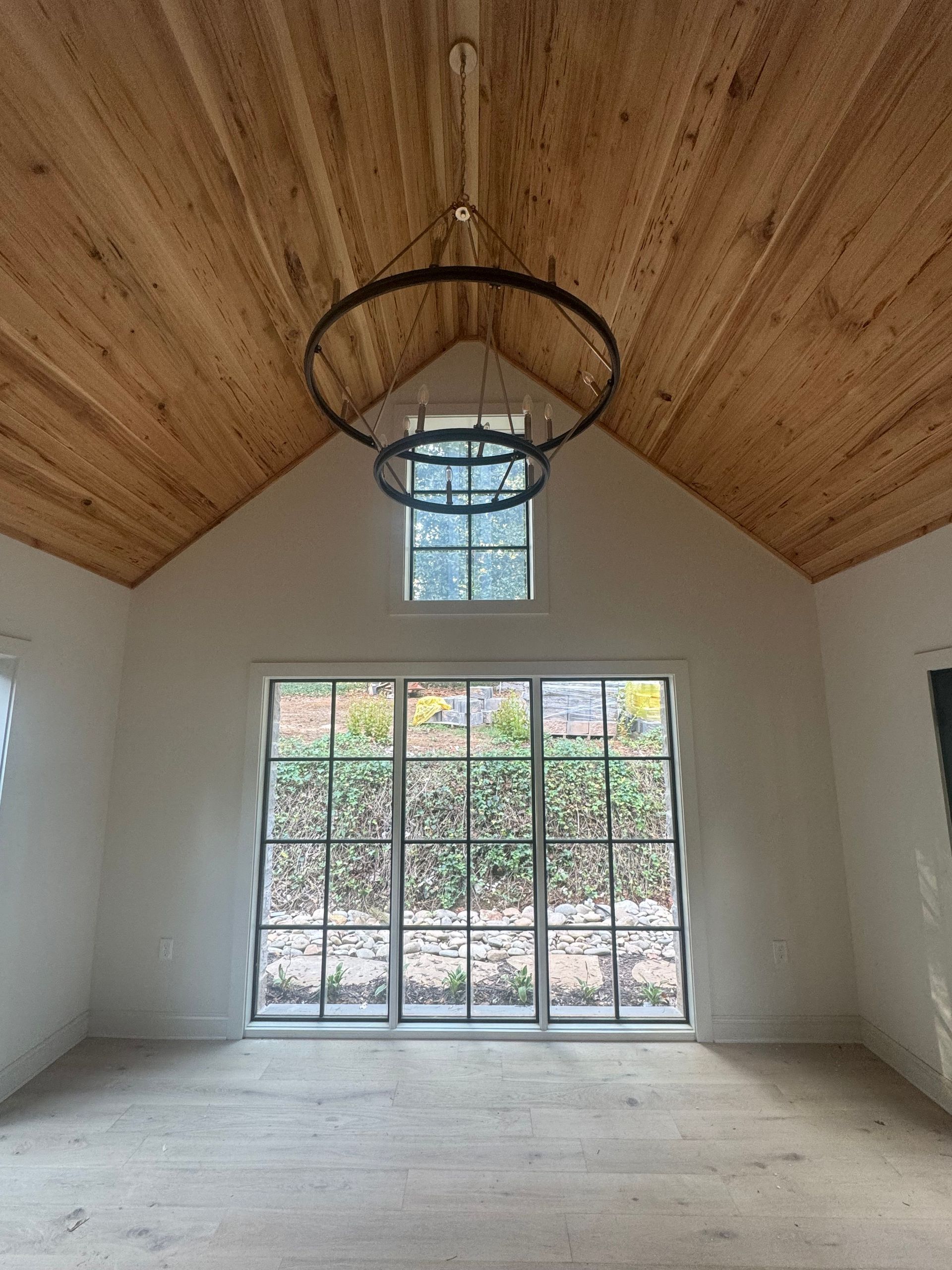 Empty room with a vaulted wood ceiling, hanging light fixture, and large glass doors to a garden.