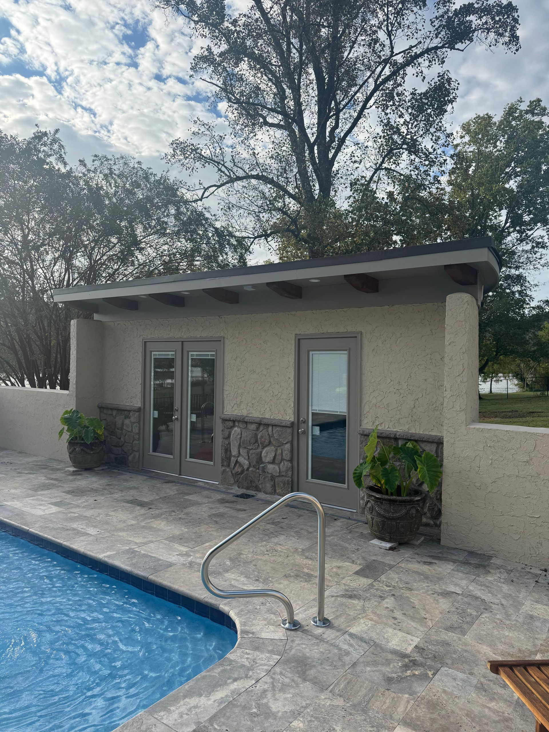Poolside cabana with glass doors and windows beside a swimming pool, surrounded by trees.