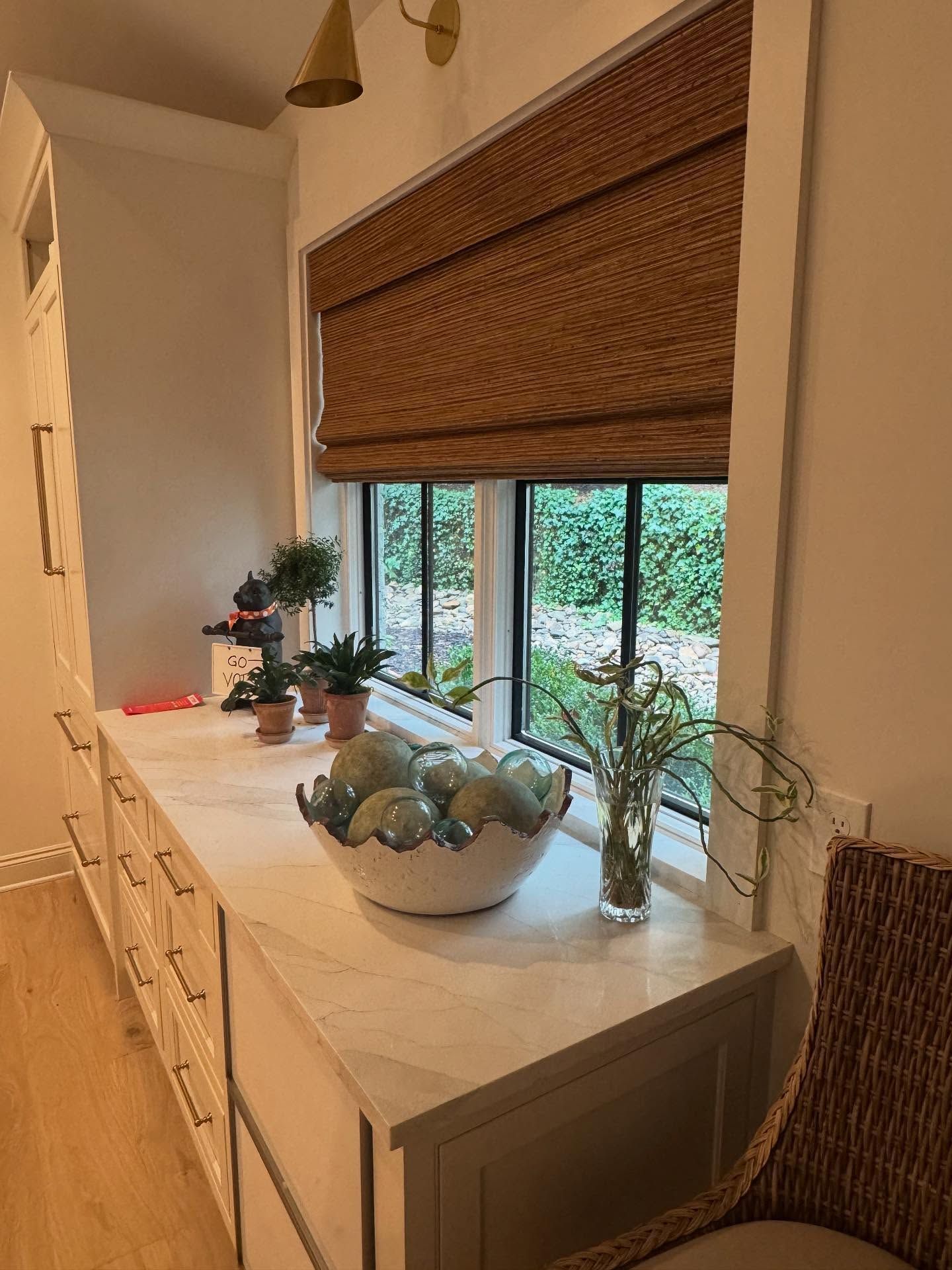 Window seat with woven blind, potted plants, and decorative bowls in a bright room