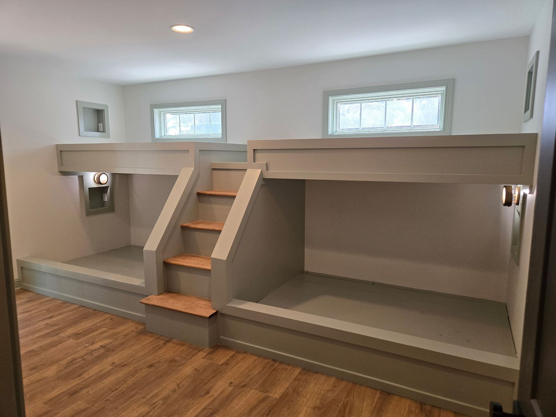 Empty room with gray bunk bed built into the wall and wooden steps in a basement setting
