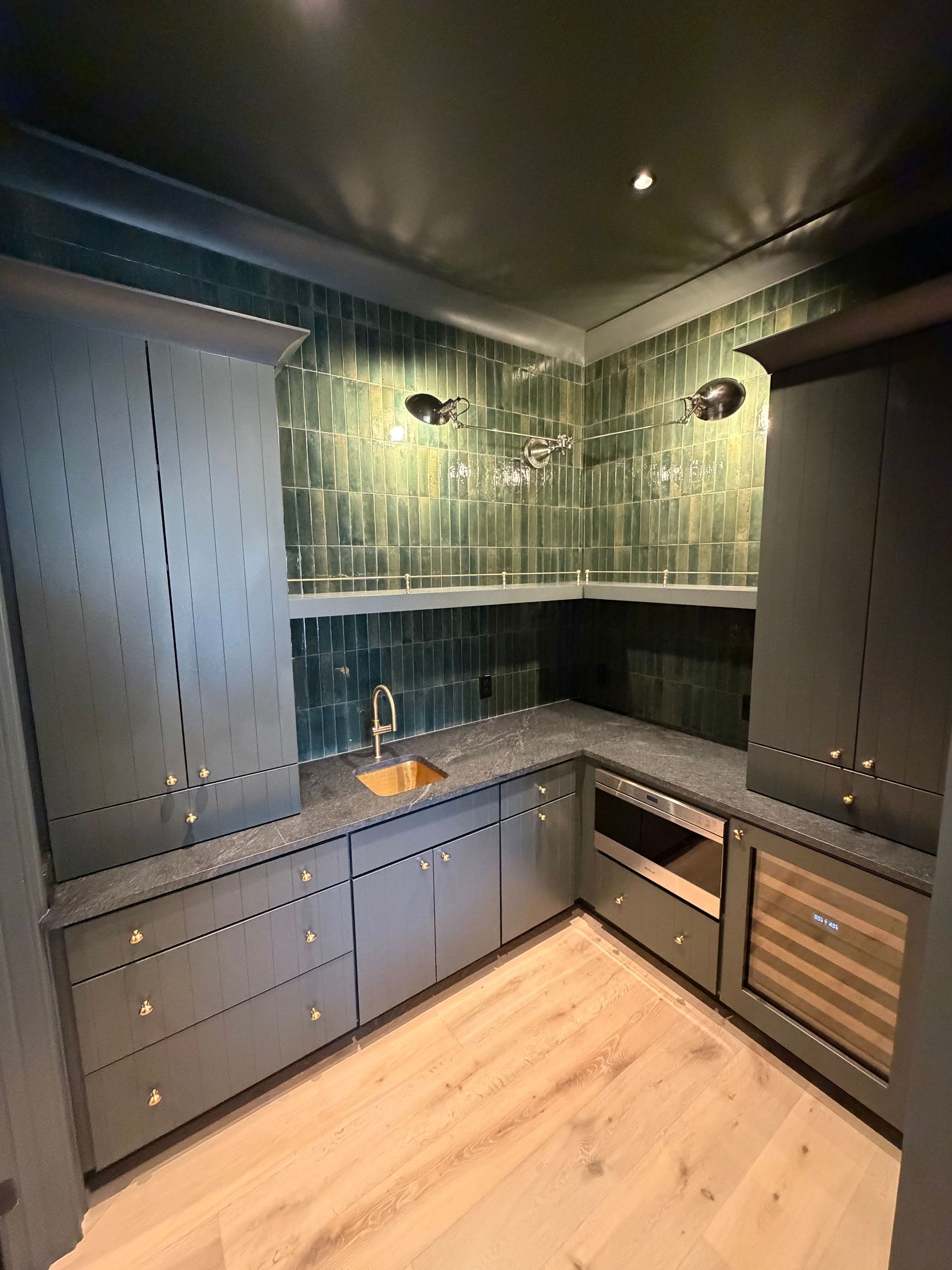Modern dark kitchen with green tile backsplash, gray cabinets, black countertop, and light wood floor