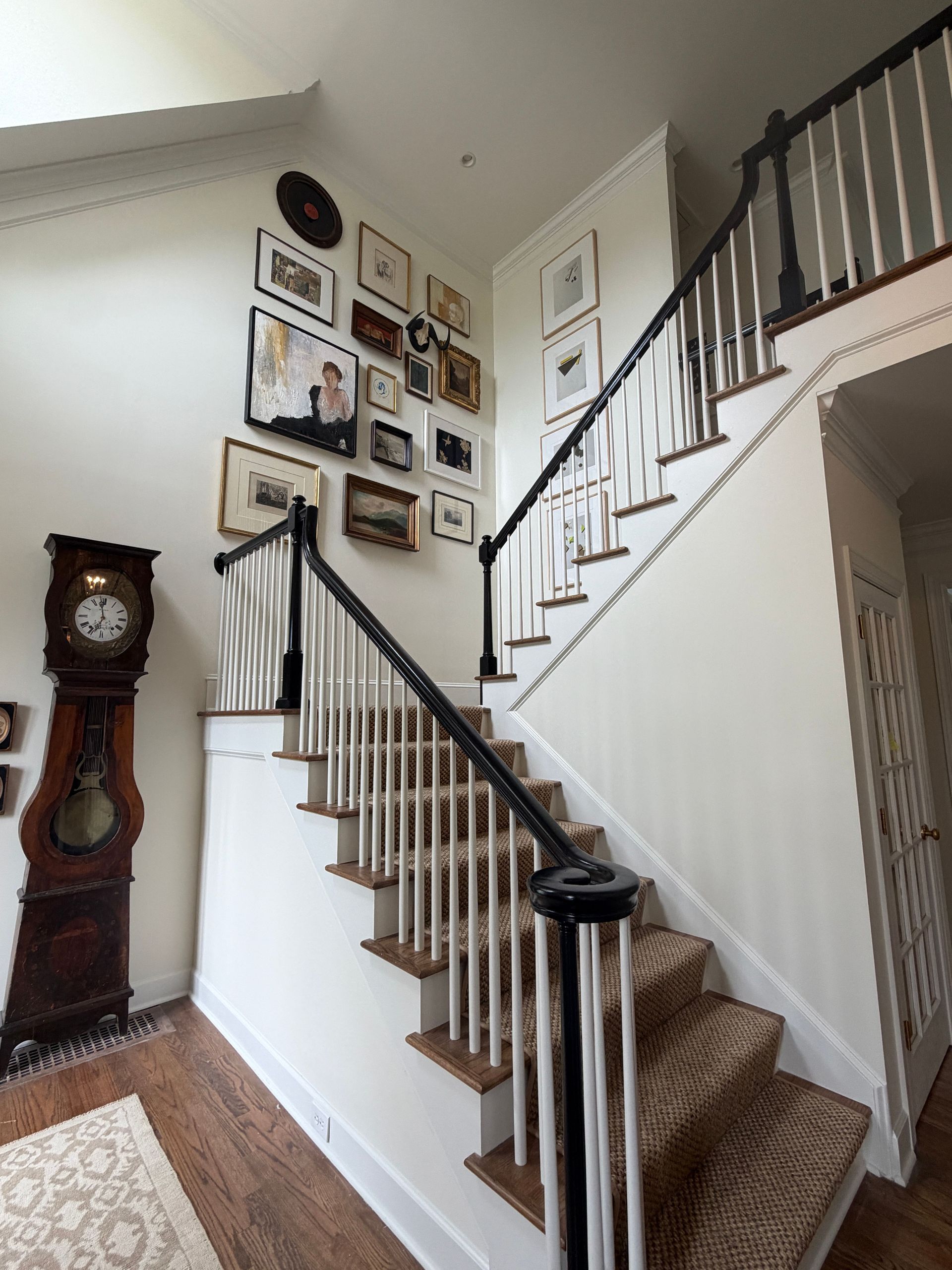 Staircase with white walls, framed photos, and a tall grandfather clock in a home foyer