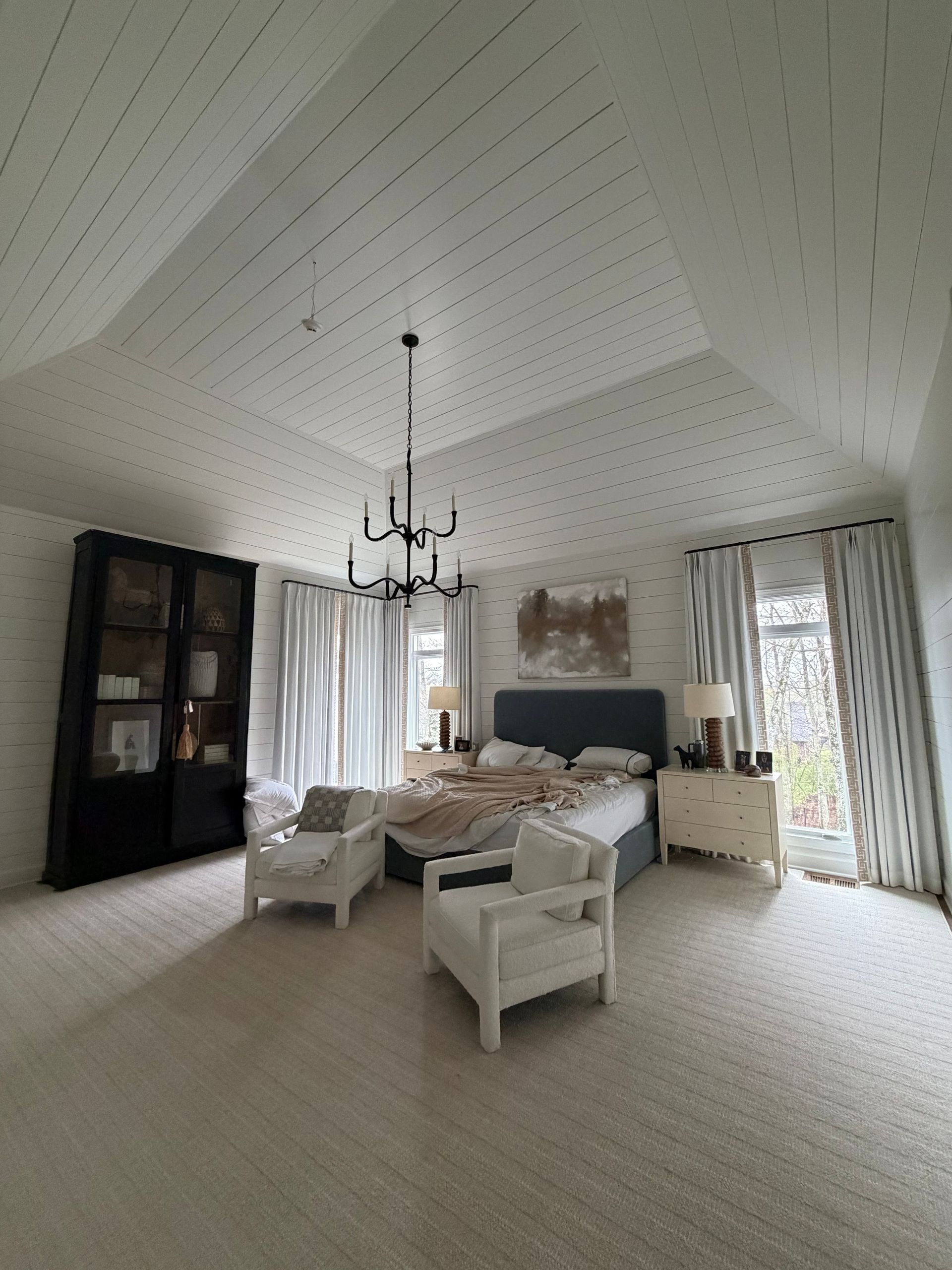 Bright, airy living room with white vaulted ceiling, chandelier, sofa, armchair, and large windows