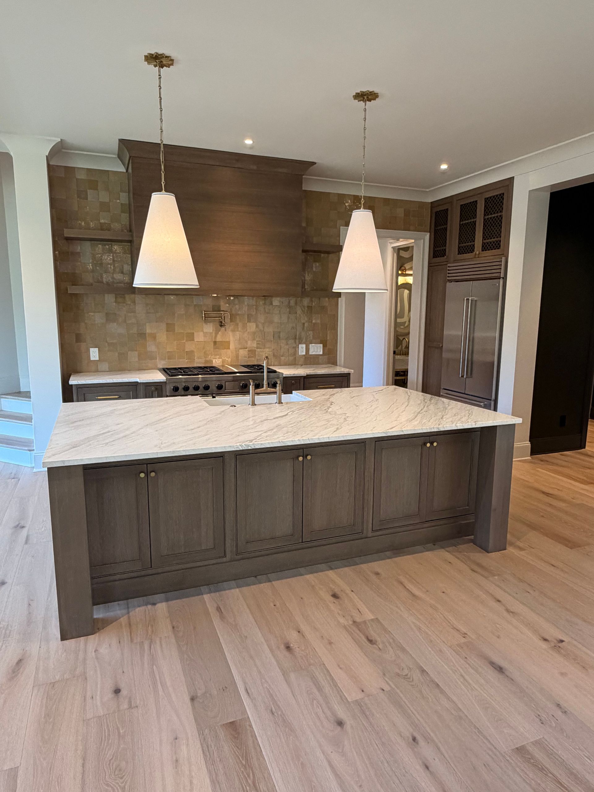 Modern kitchen with large island, light wood floors, white countertops, and pendant lights