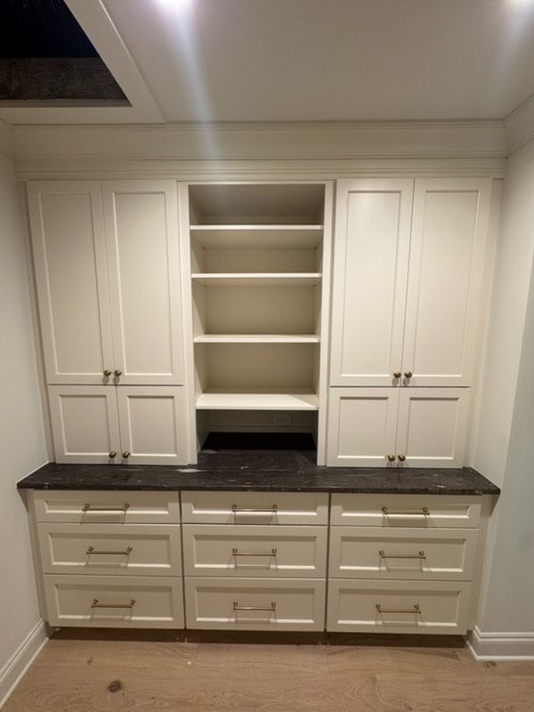 Built-in white cabinetry with open shelves and dark countertop in a hallway or utility room.