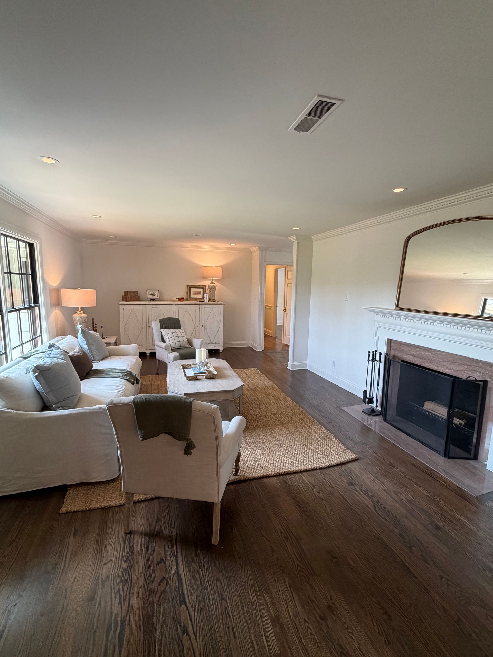 Bright living room with white sofa, fireplace, rug, and hardwood floors, softly lit by lamps and windows