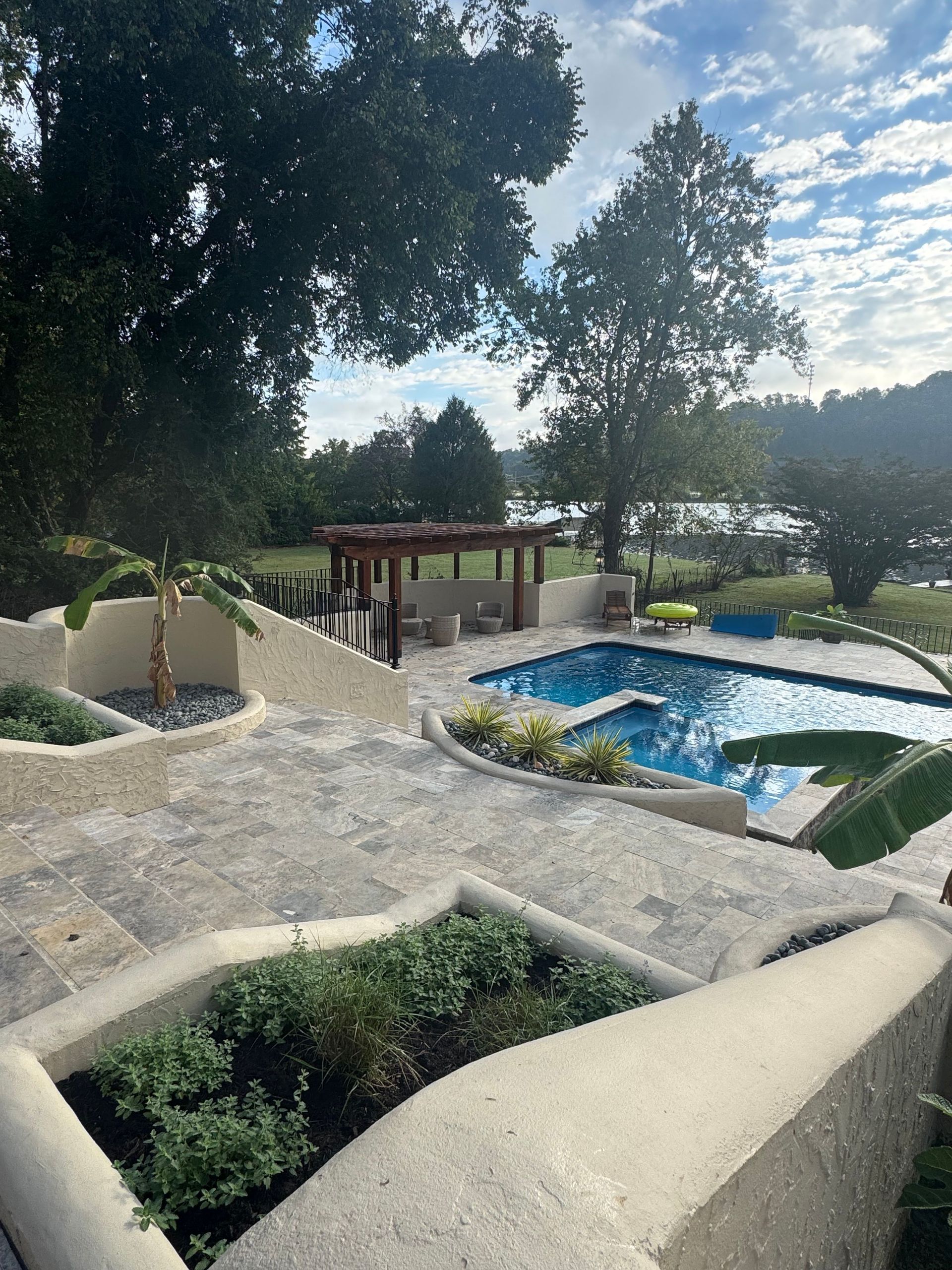 Resort pool with blue water, stone landscaping, trees, and a lakeside view under a sunny sky