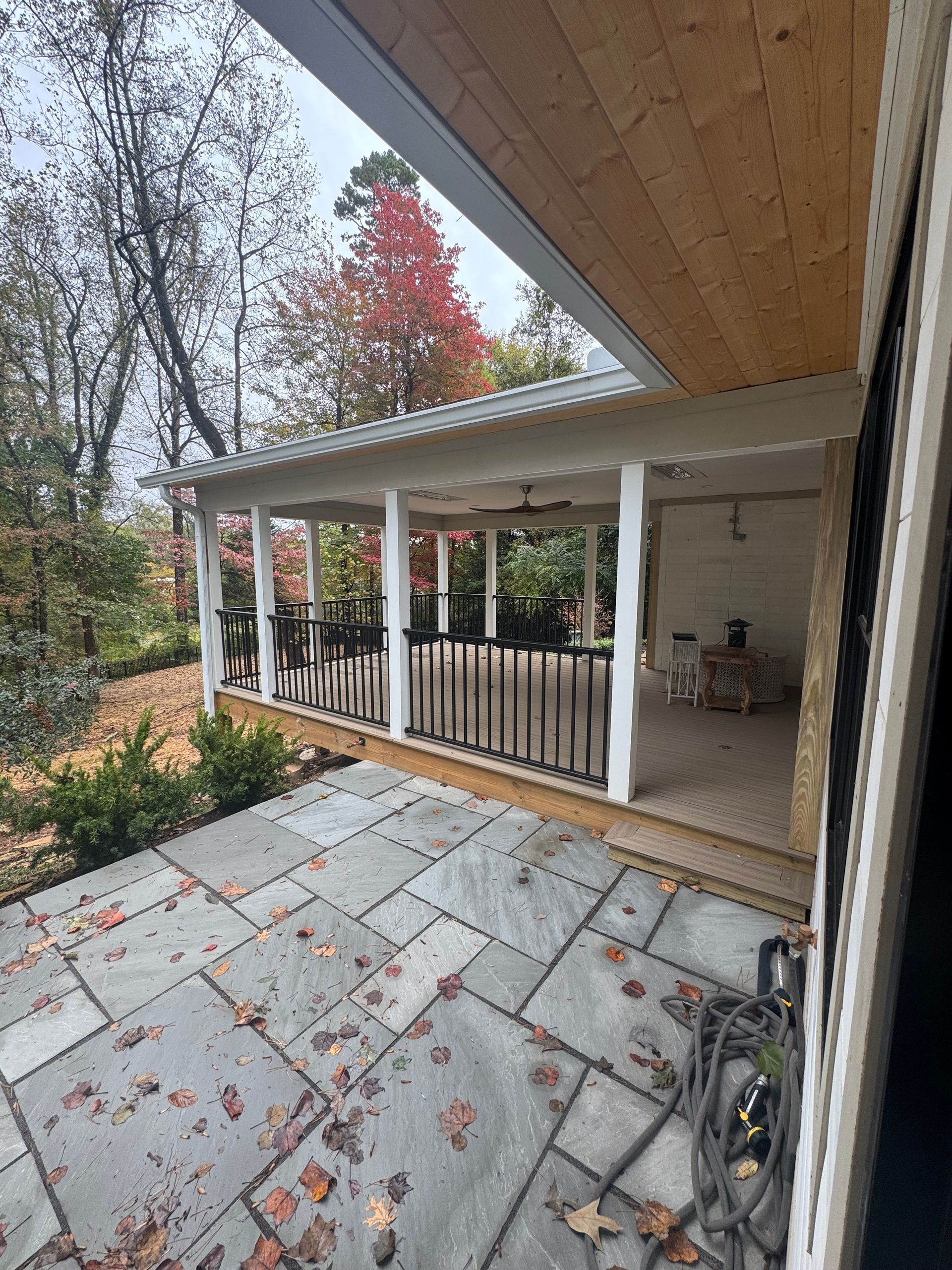 Covered patio with white columns overlooking a stone terrace and autumn trees