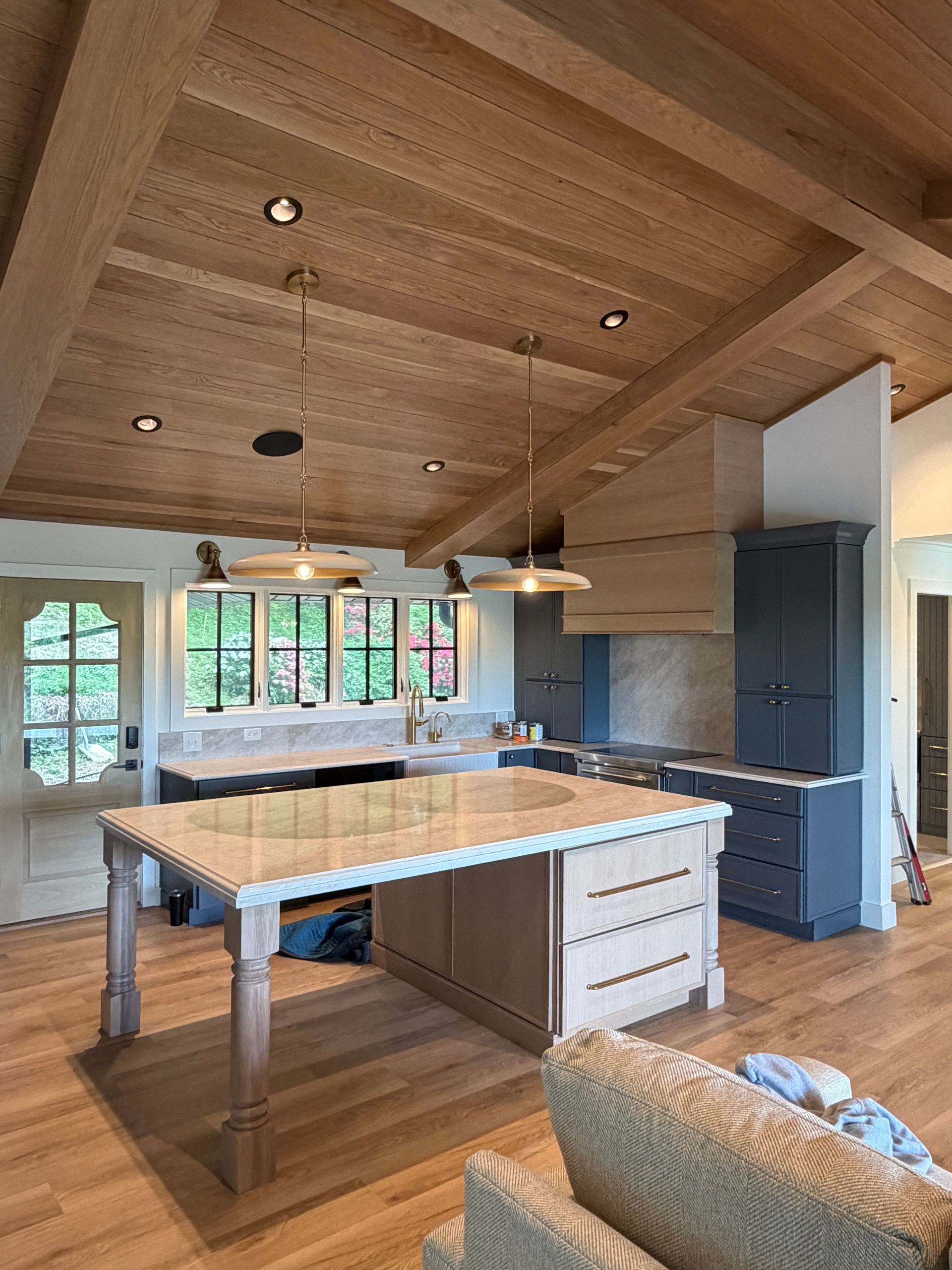Modern kitchen with wood-paneled ceiling, large island, pendant lights, and dark cabinets