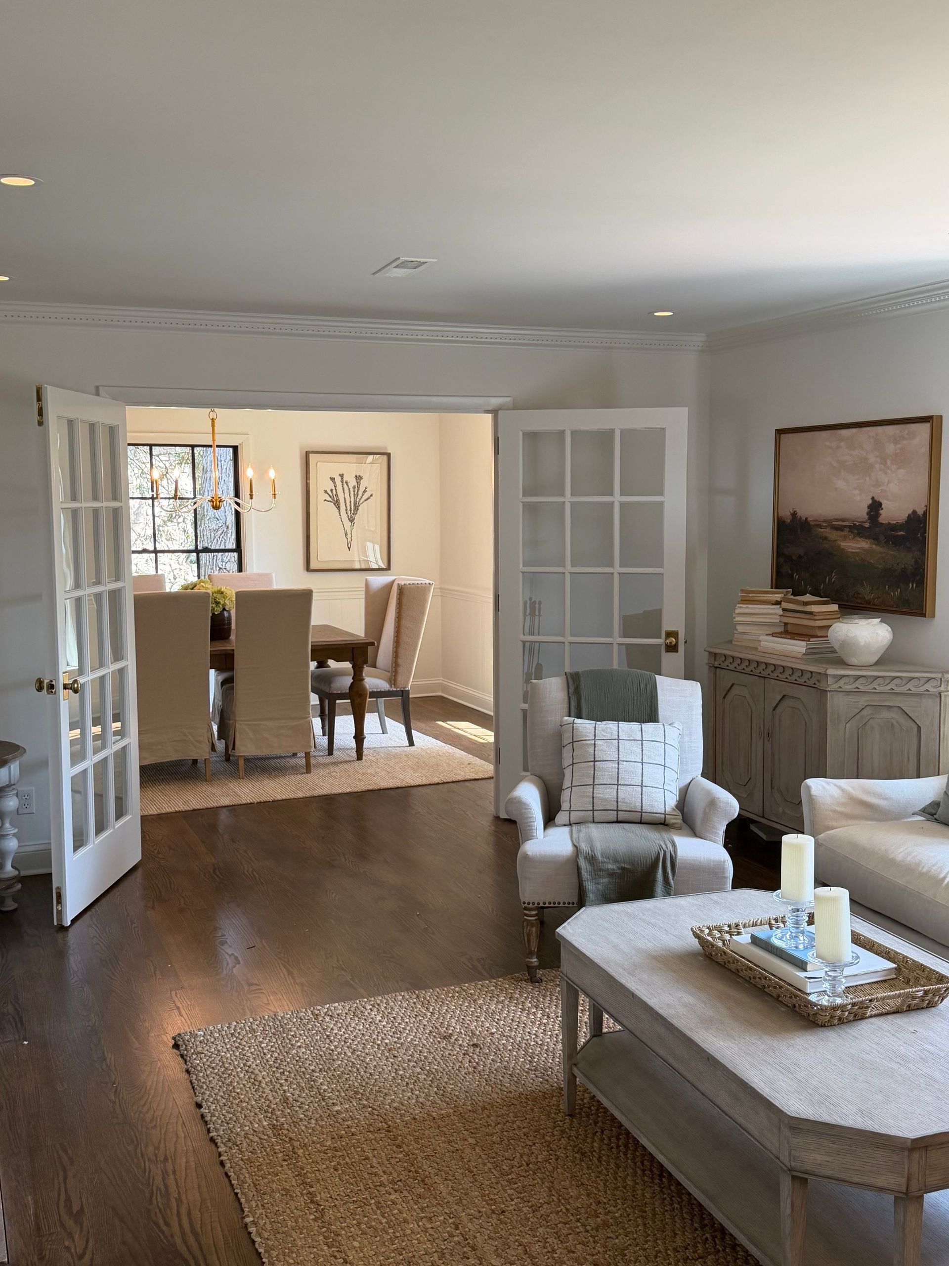 Bright living room with white chairs, woven rug, coffee table, and open doors to a dining area