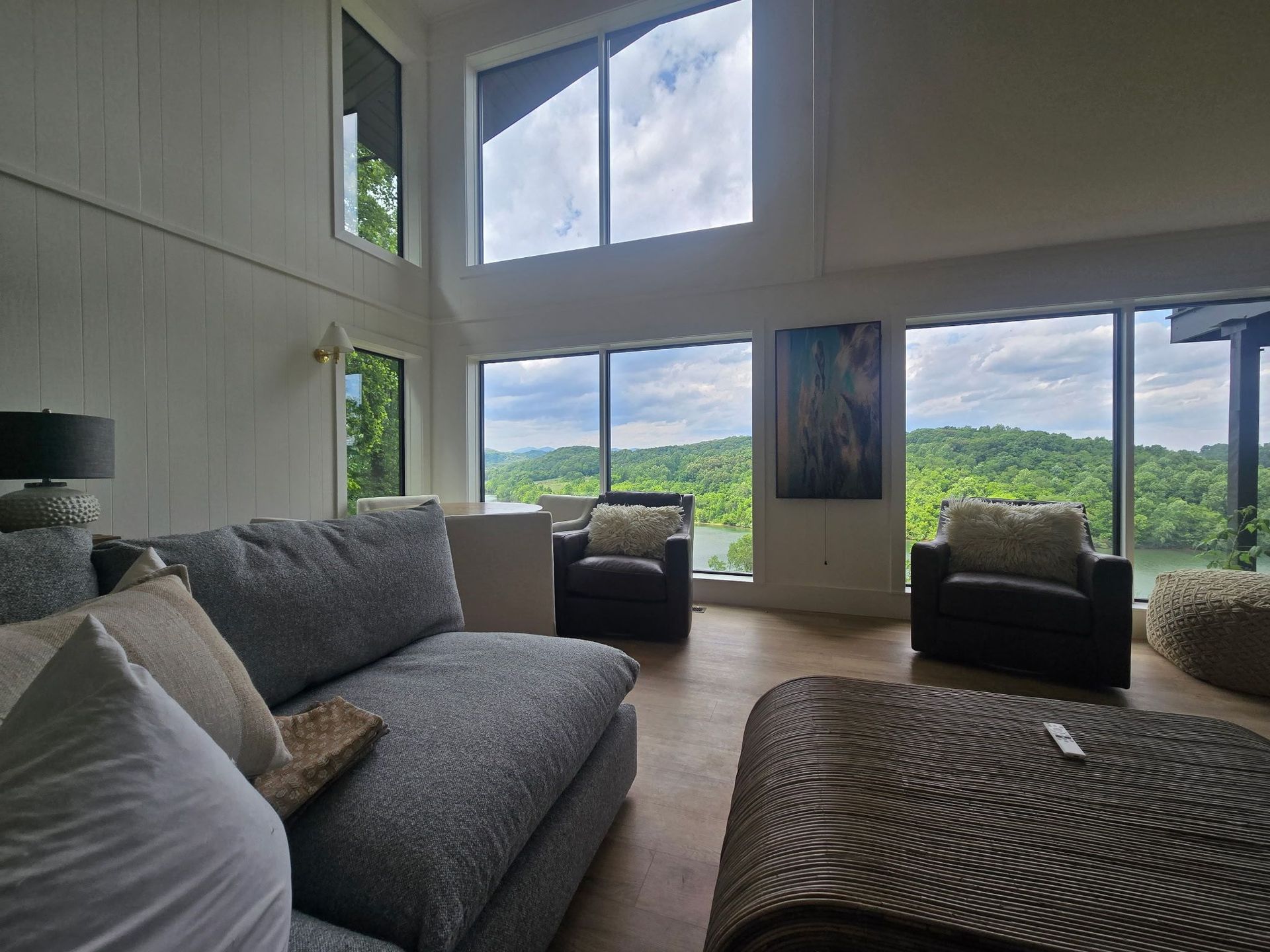 Bright living room with gray sofas, large windows, and a scenic green landscape outside.