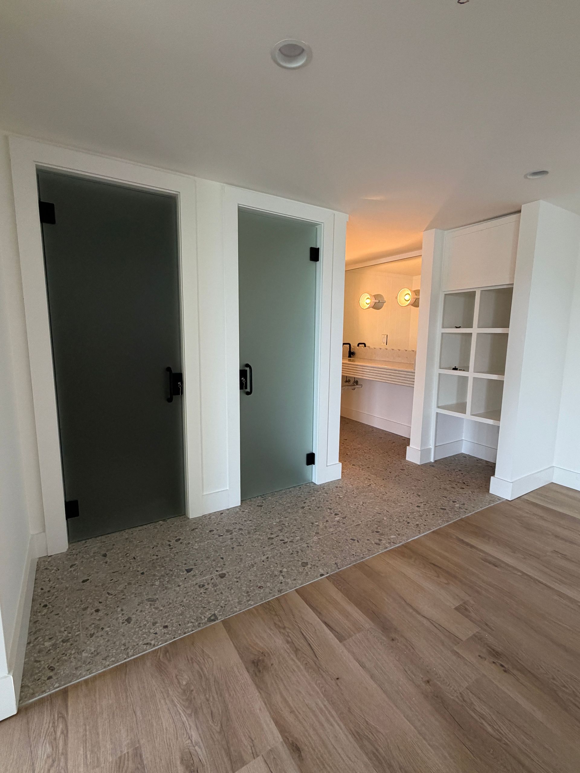 Modern hallway with two dark sliding doors, white walls, wood flooring, and a bright bathroom in the back.