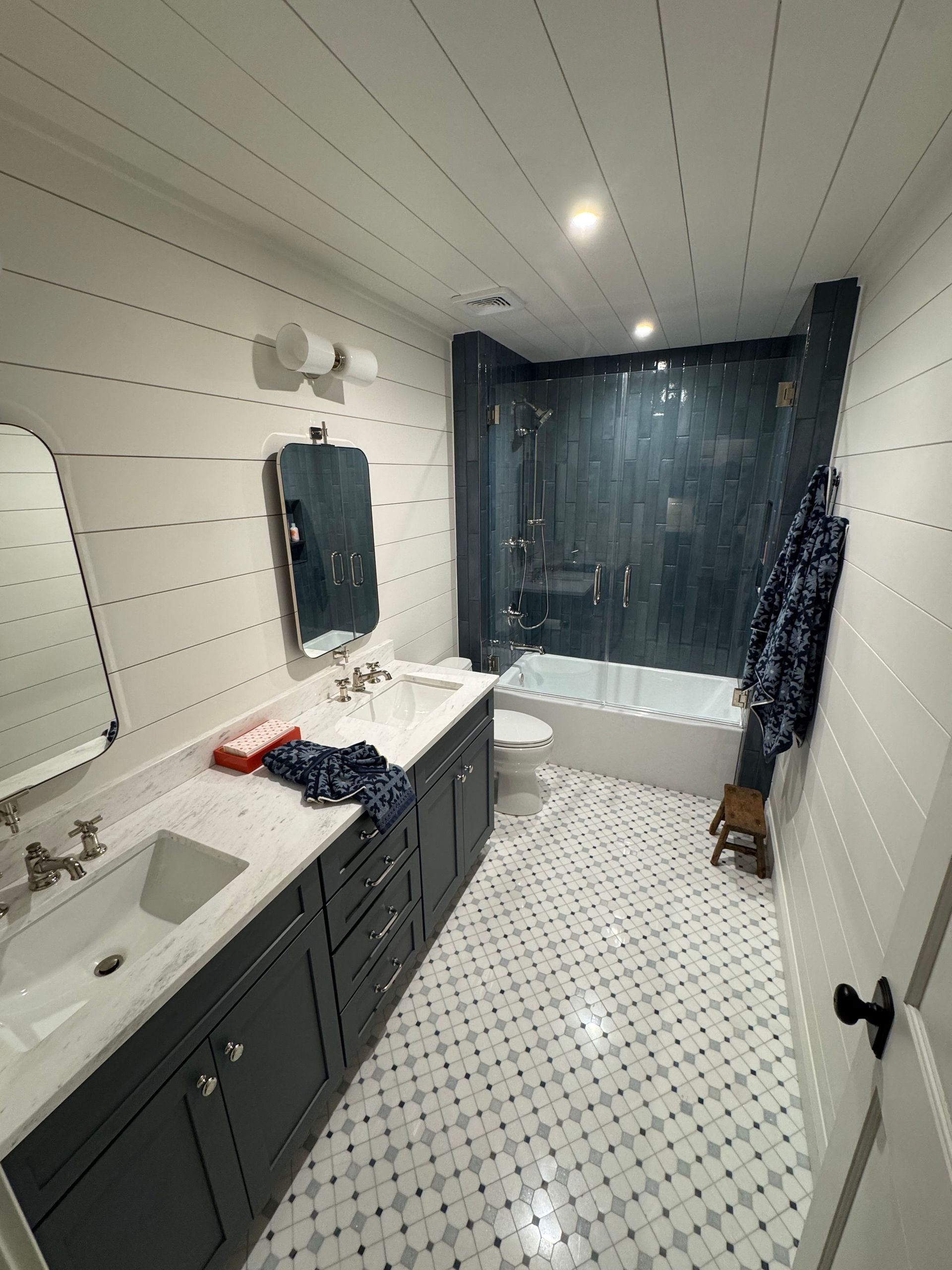 Narrow bathroom with double sinks, dark vanity, tiled floor, and shower curtain at the back.
