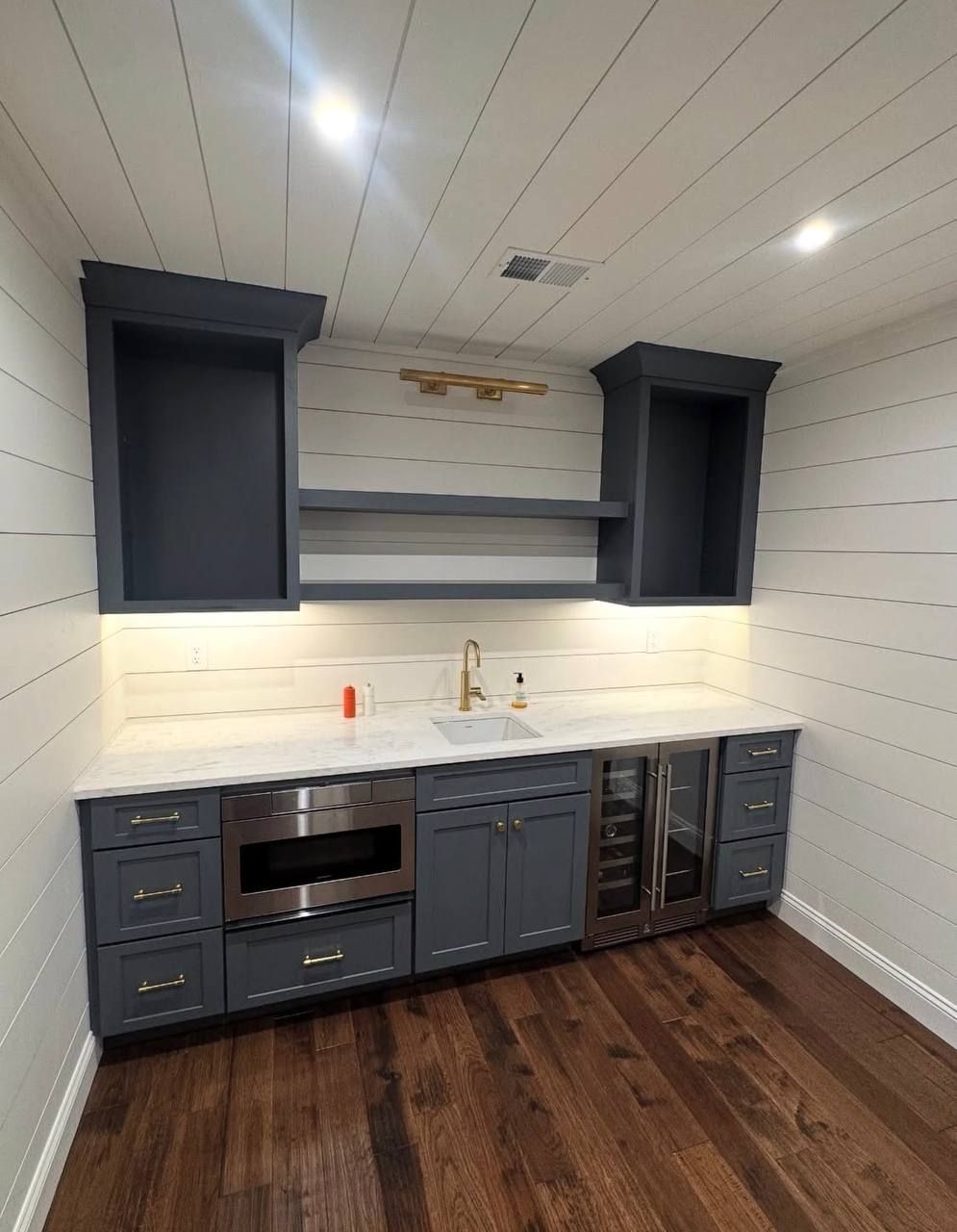 Modern kitchen with dark gray cabinets, white shiplap walls, wood floor, and built-in oven.