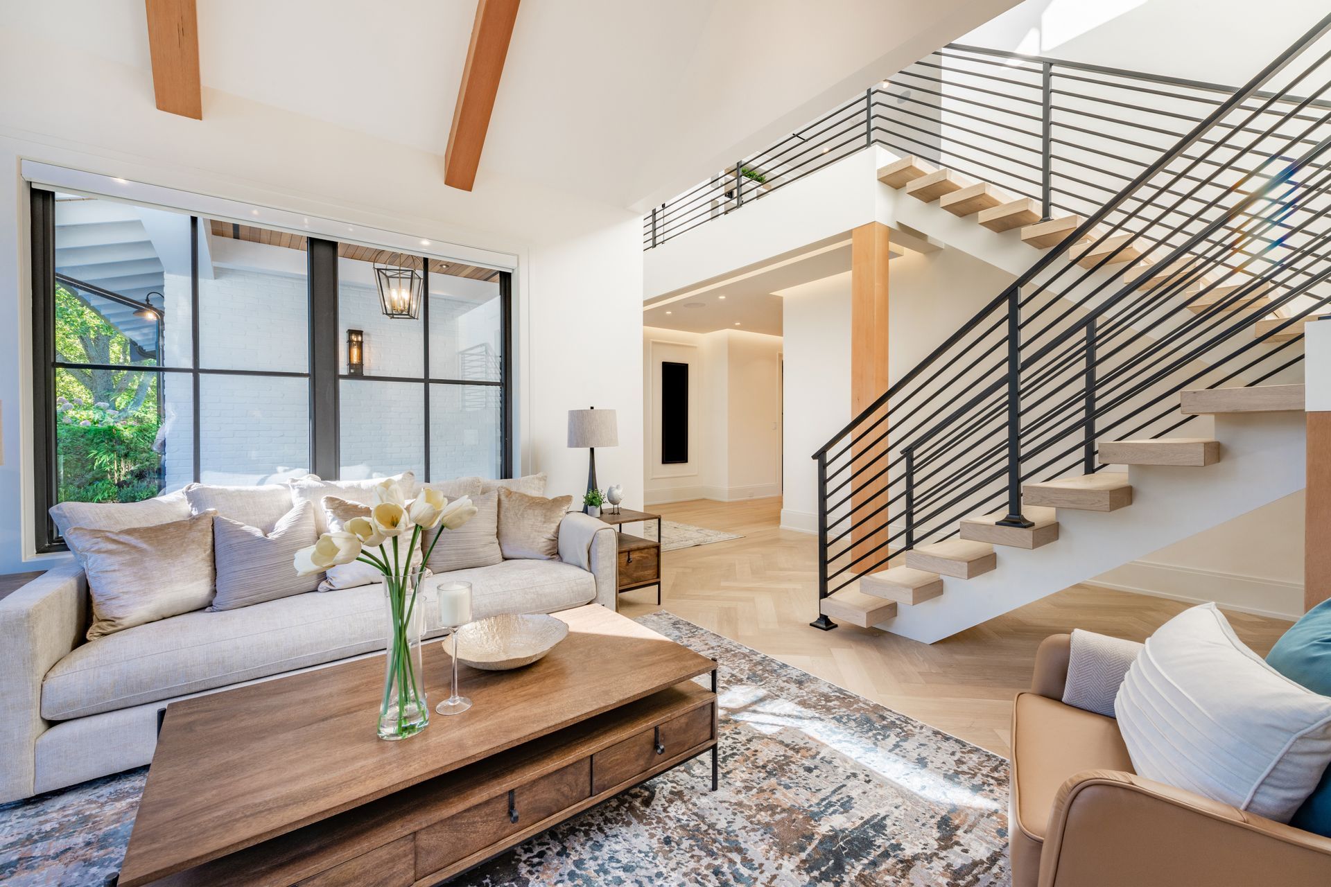 Bright modern living room with gray sofas, wooden coffee table, and open staircase with black railing