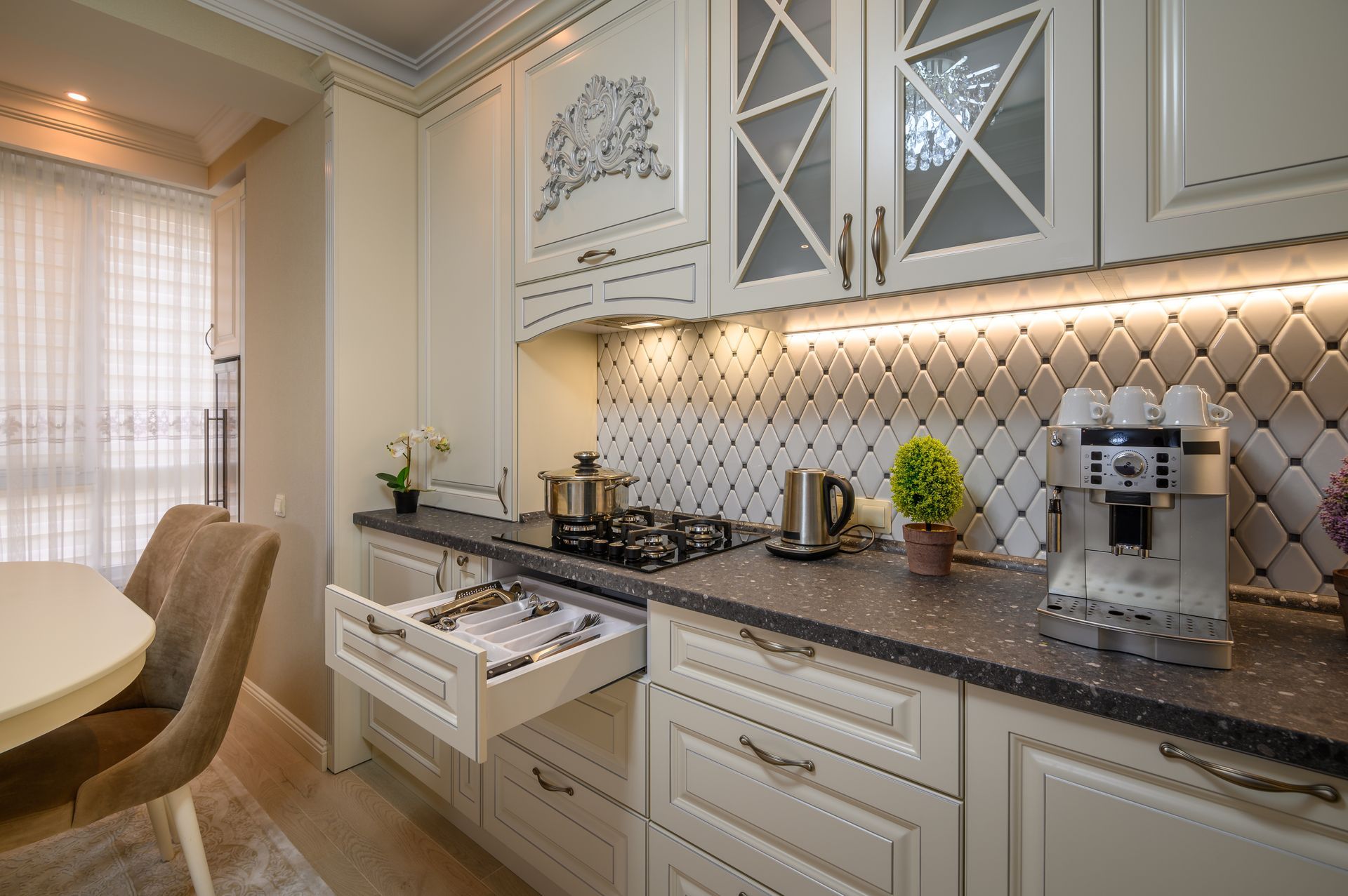 Bright cream kitchen with marble counters, open drawer, gas stove, and coffee machine by a tiled backsplash