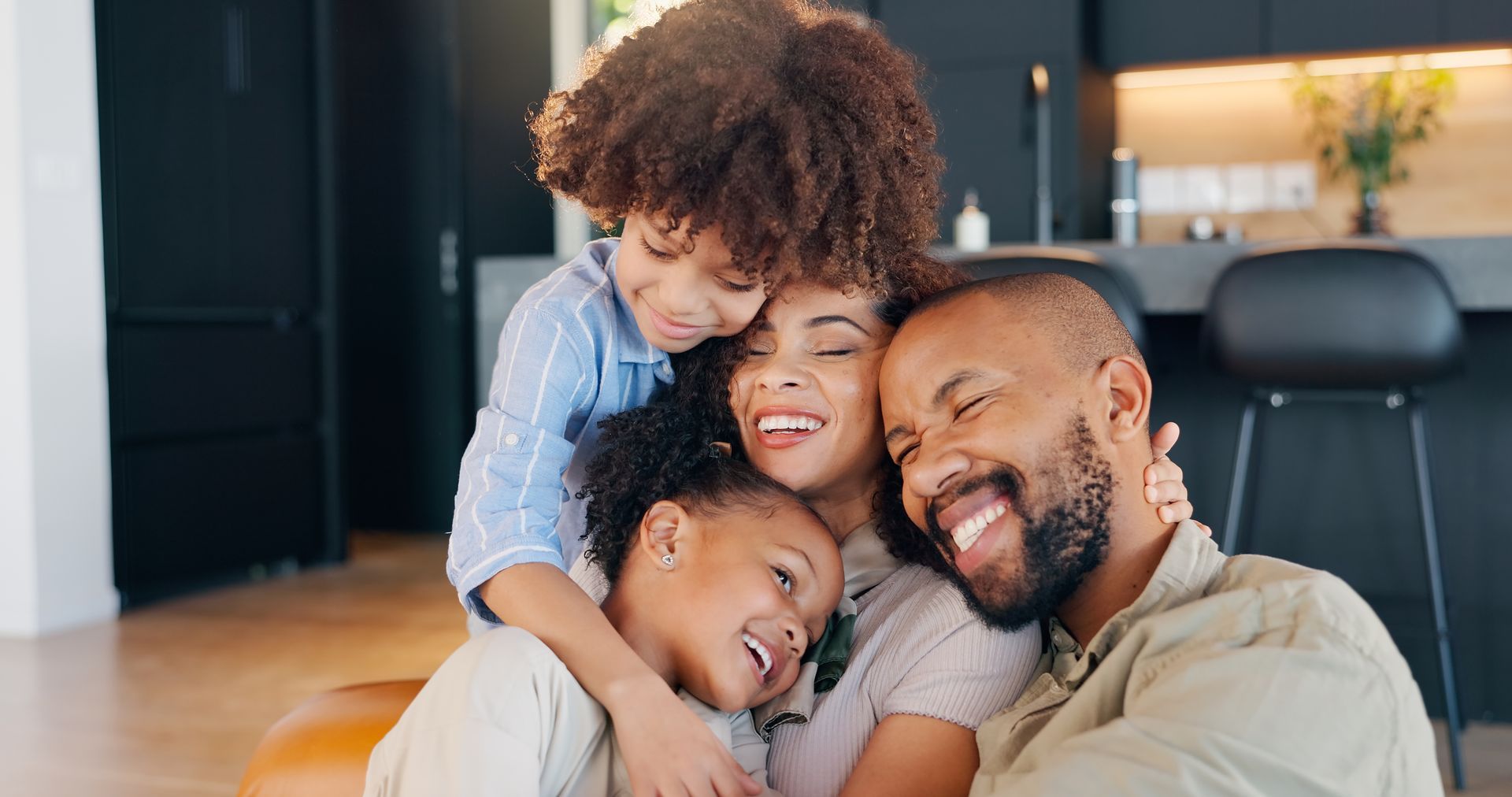 Smiling family hugging on a living room floor, with warm, cozy lighting.