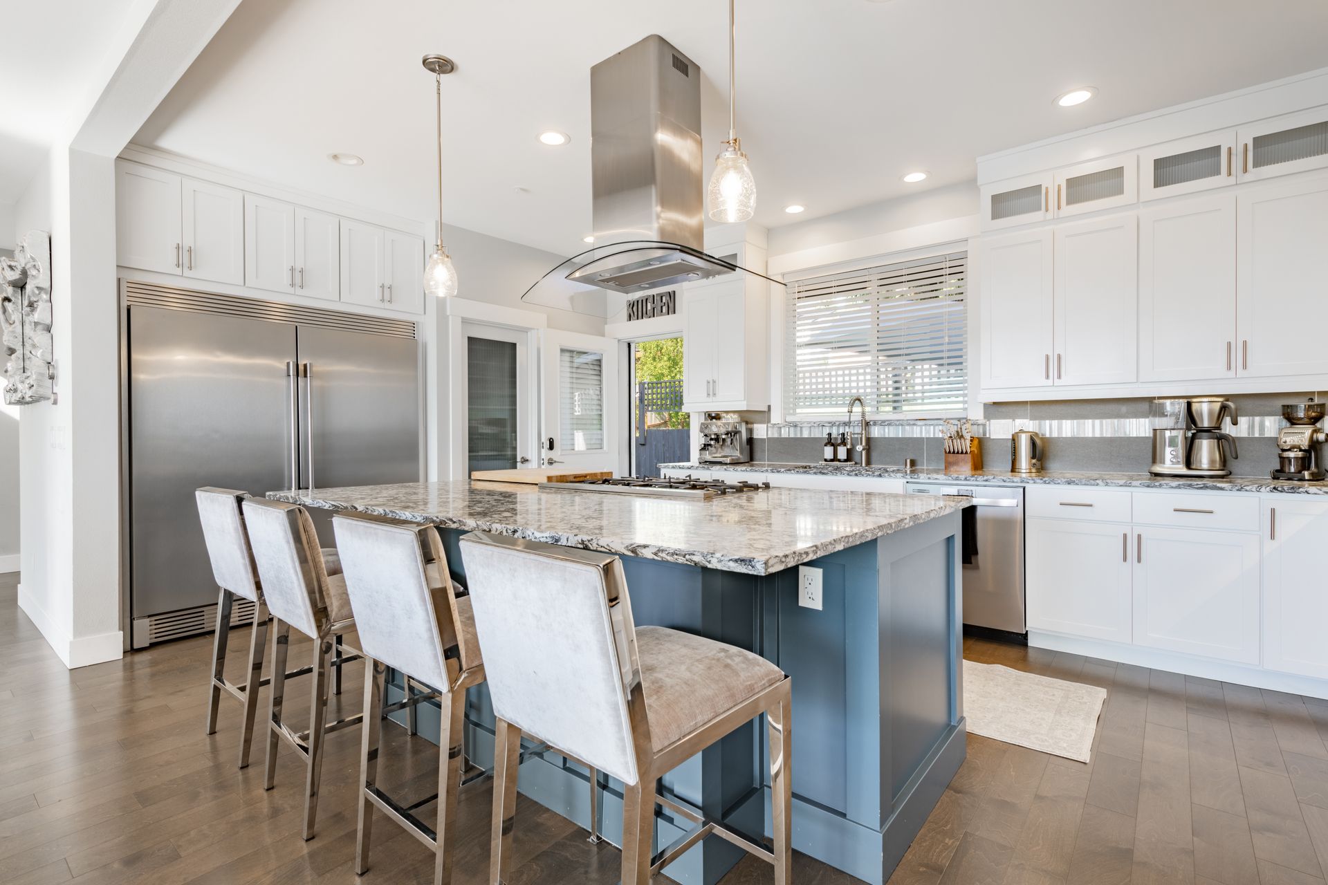Bright modern kitchen with white cabinets, stainless appliances, and blue island with bar stools