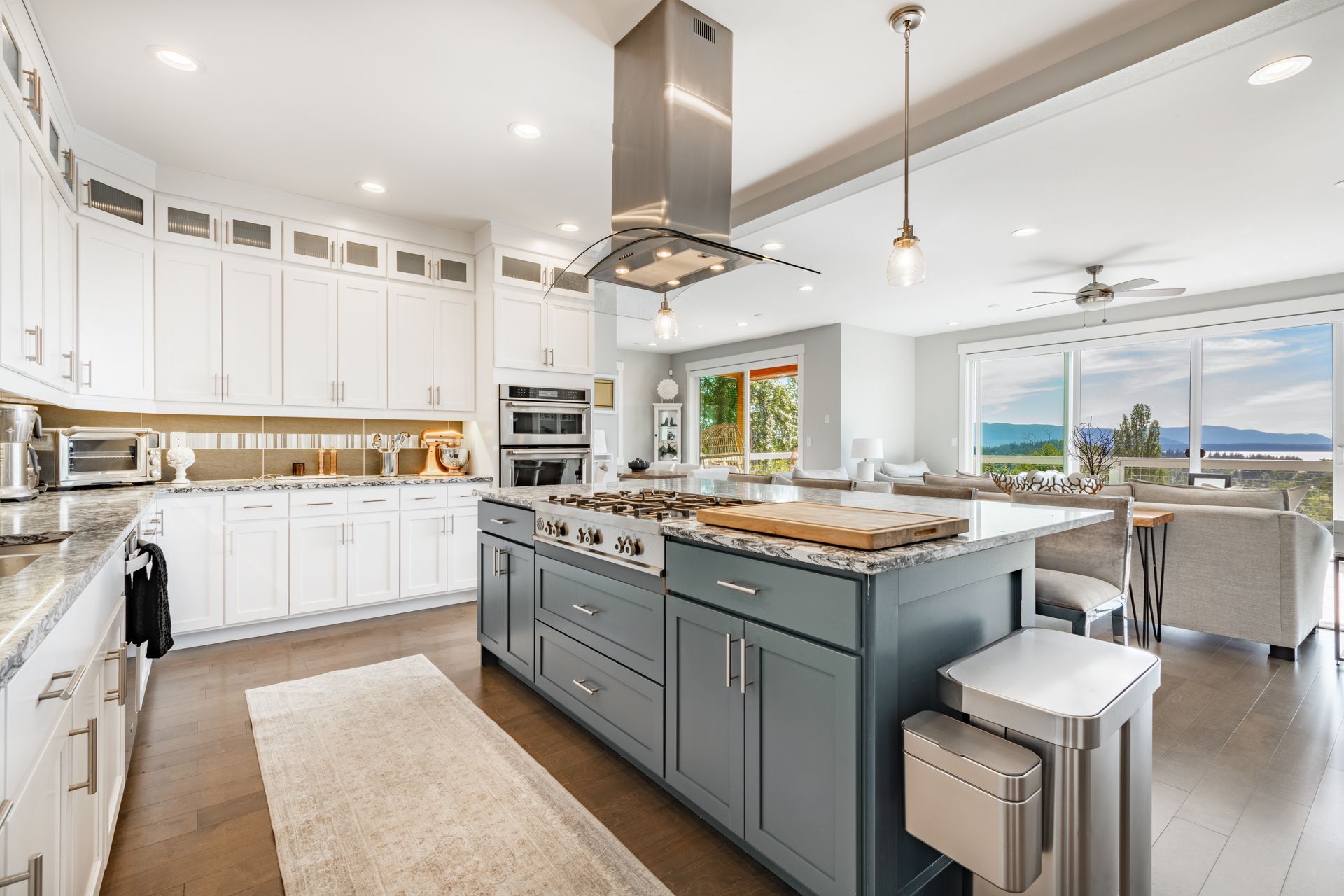 Bright modern kitchen with white cabinets, teal island, stainless appliances, and ocean-view dining area
