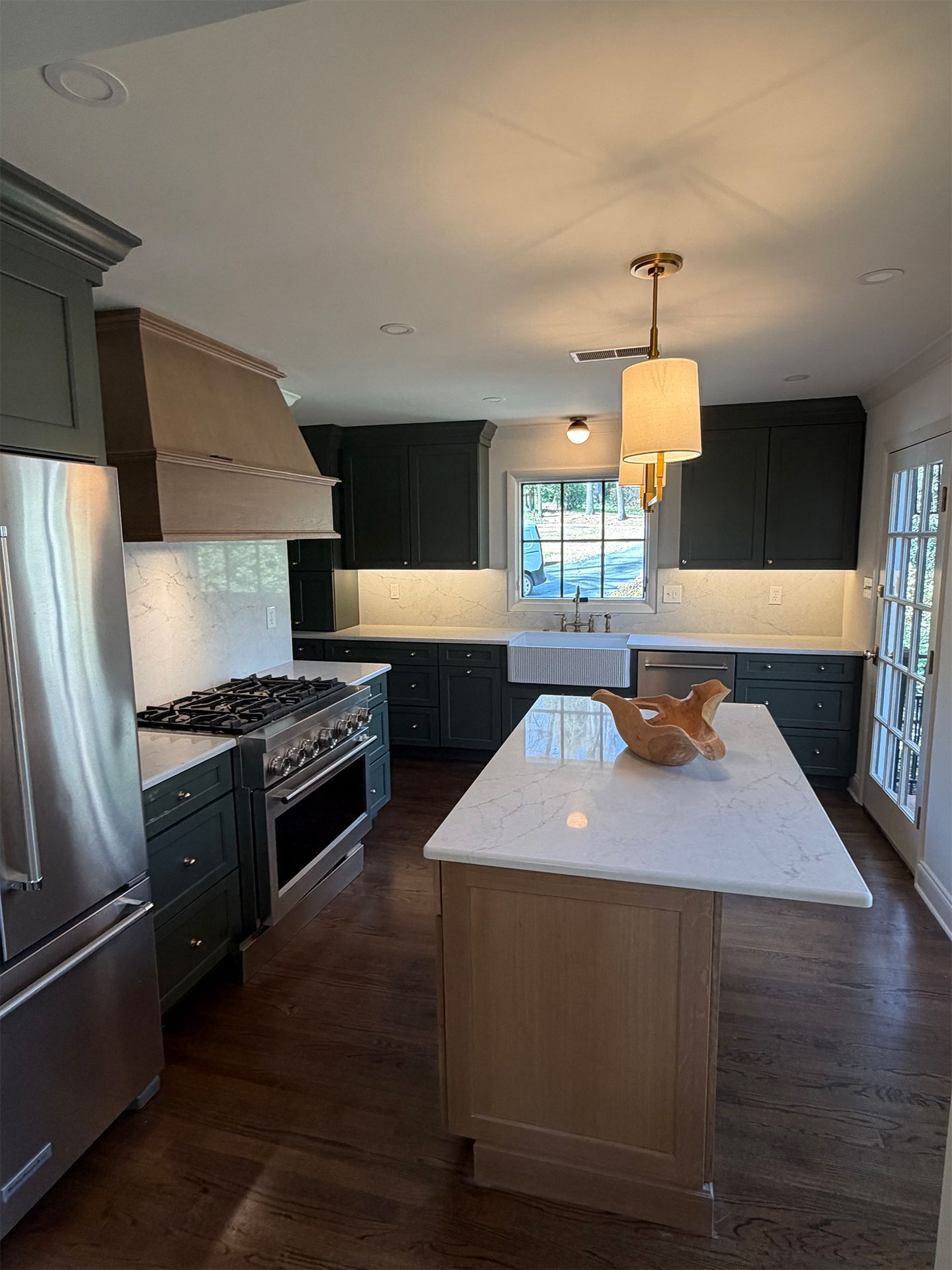 Modern kitchen with dark cabinets, stainless appliances, and a large white island under a pendant light