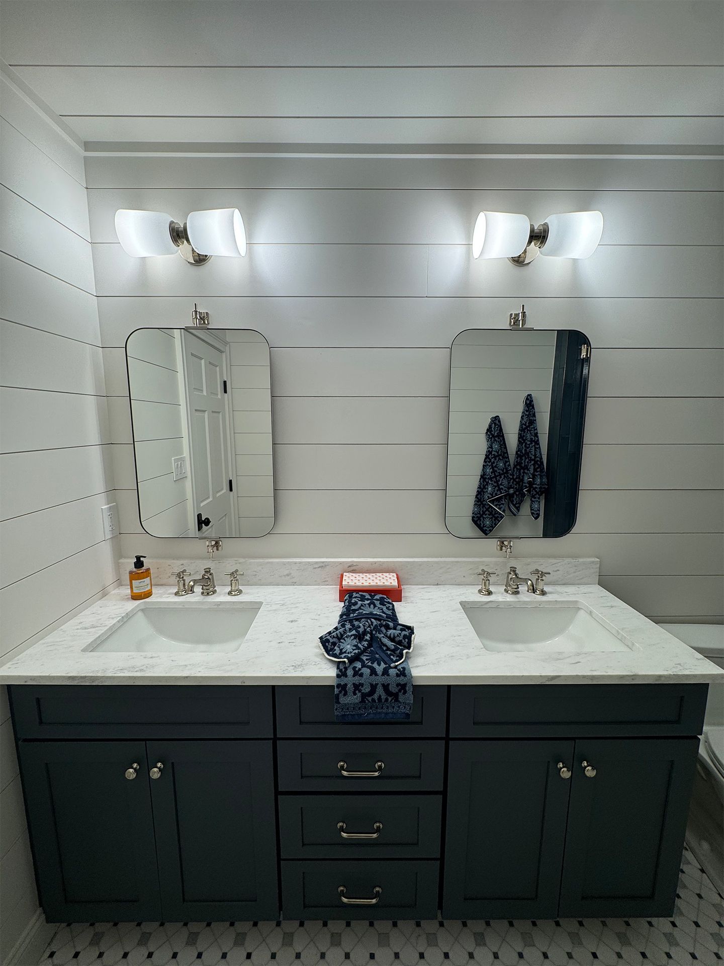 Double vanity bathroom with dark cabinets, two mirrors, wall sconces, and striped shiplap wall.