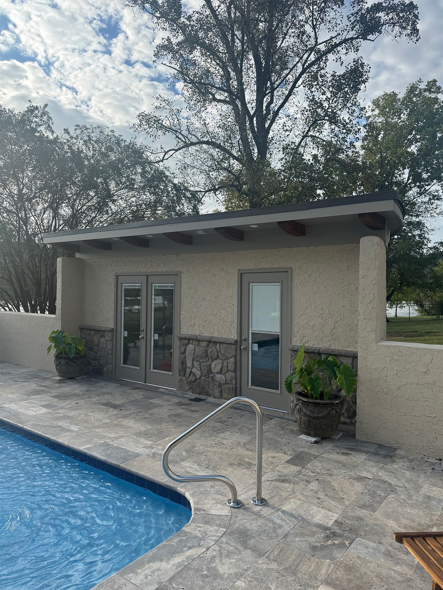 Poolside patio with a small stucco building, glass doors, and a metal handrail beside the pool