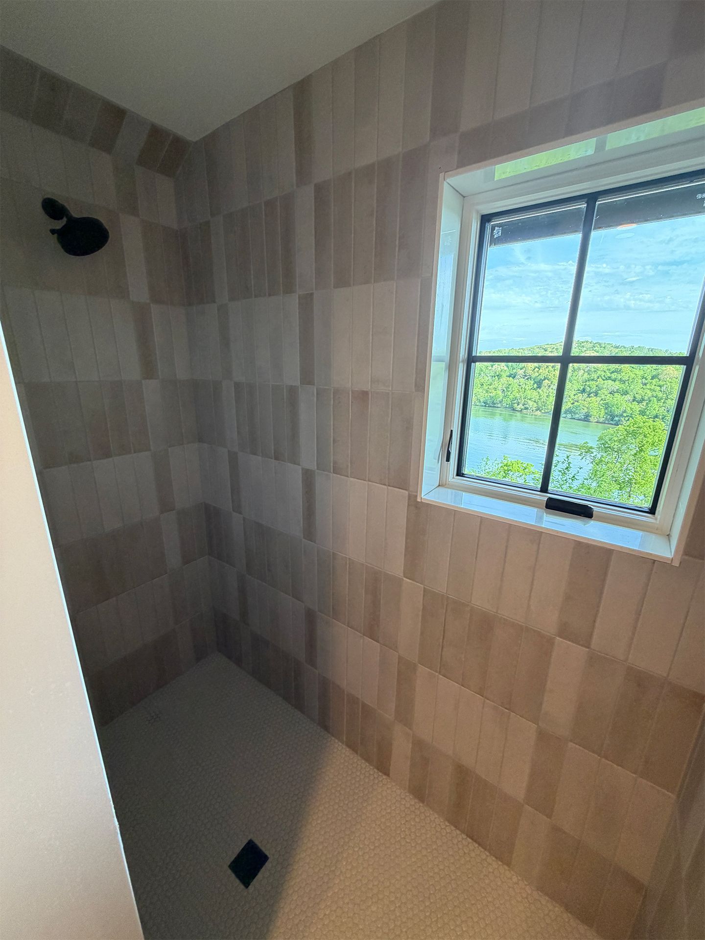 Small tiled shower room with a window and wall-mounted showerhead, beige and gray tiles.