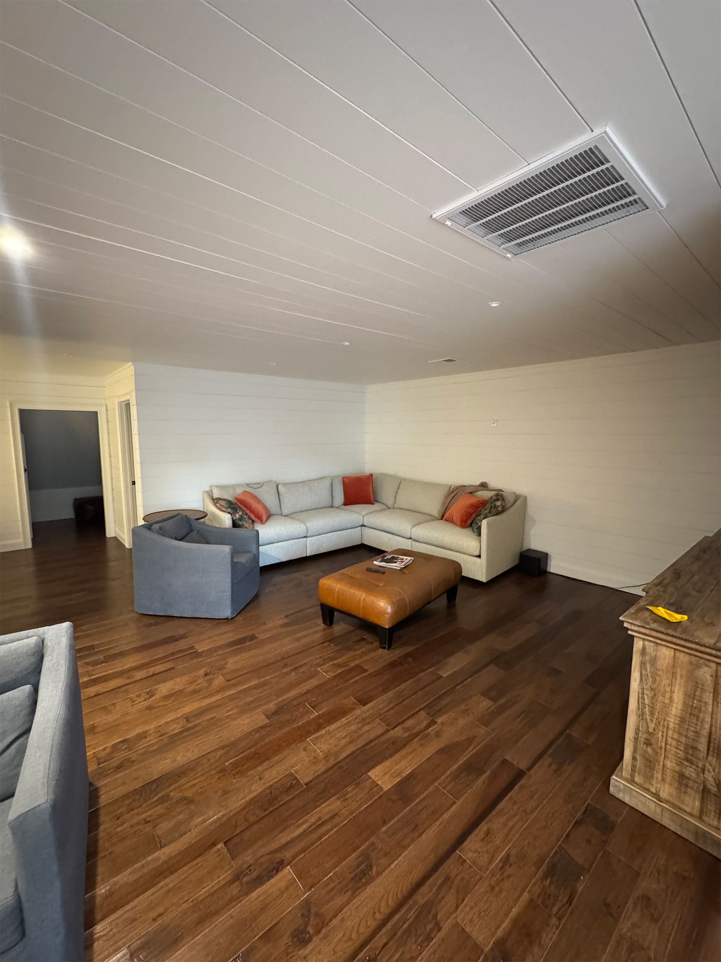 Cozy living room with gray sectional, orange pillows, wooden coffee table, and hardwood floor.