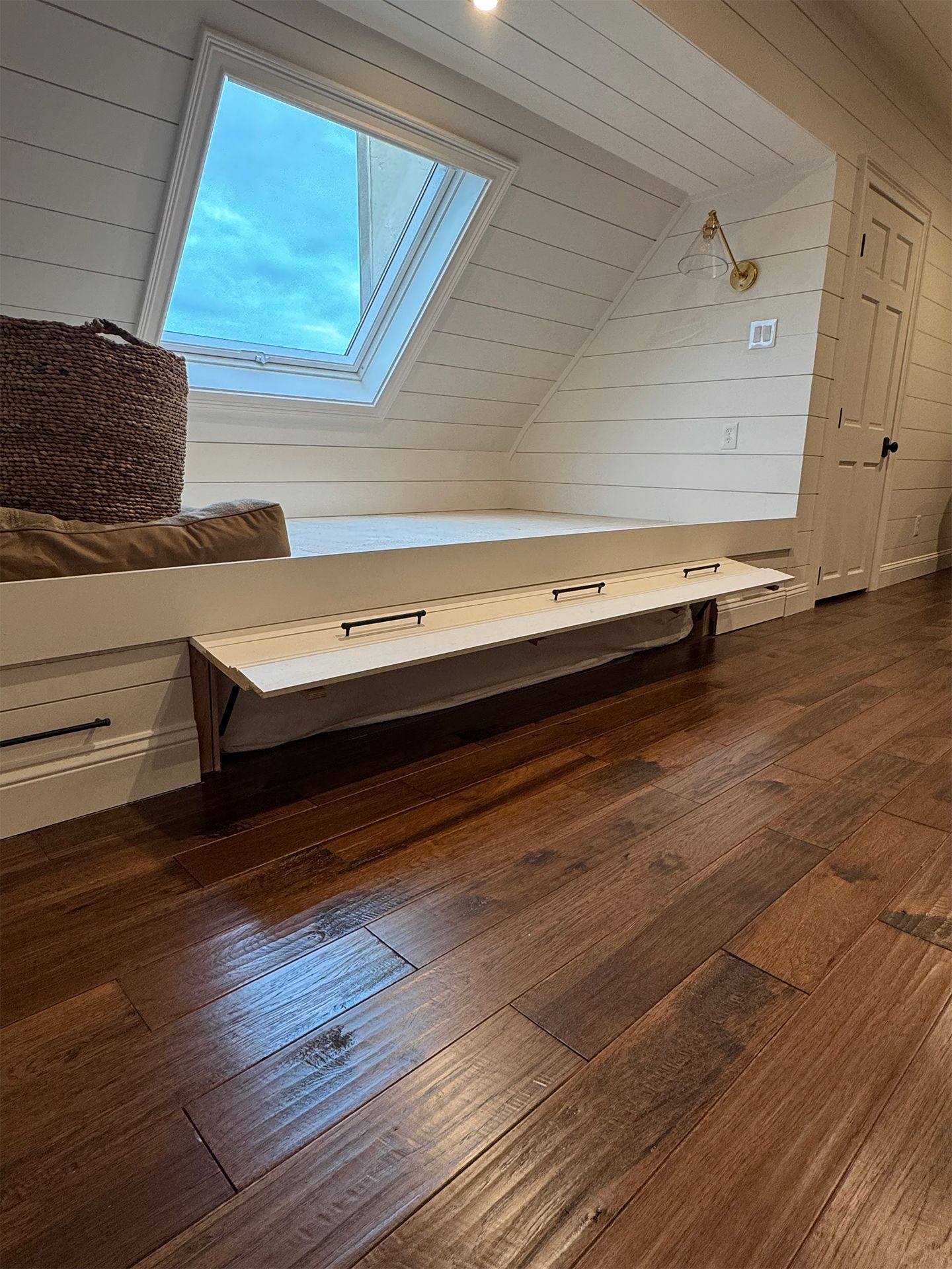 Attic bedroom with skylight window, wooden floor, and low white bed by the wall.