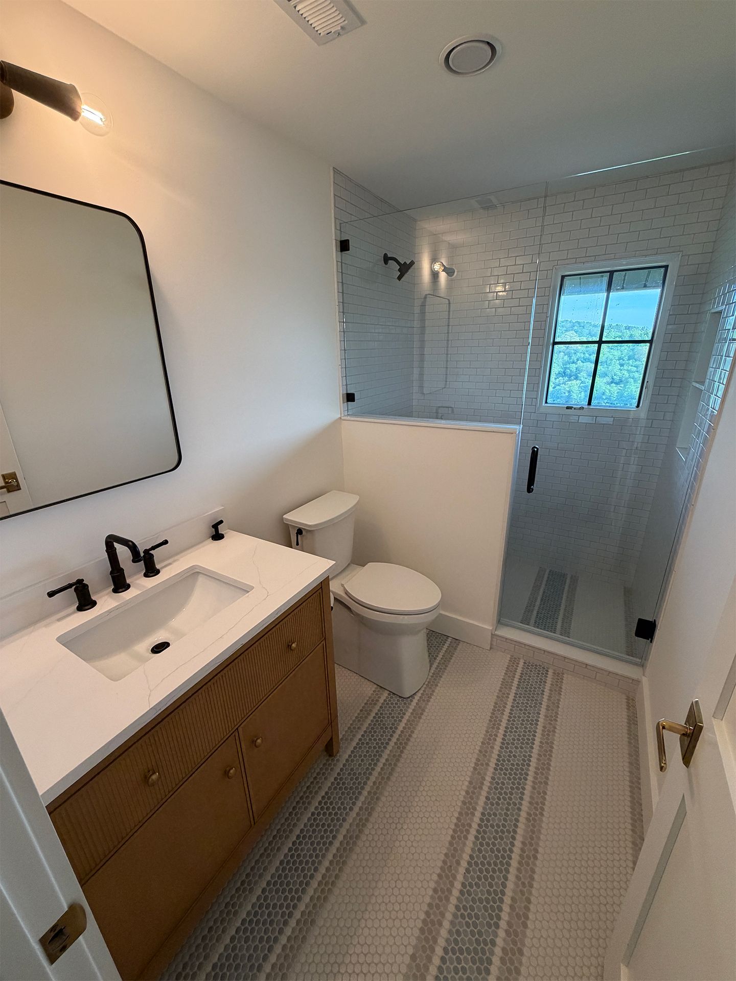 Small bathroom with vanity, toilet, and glass shower; white tile walls and beige patterned floor runner.