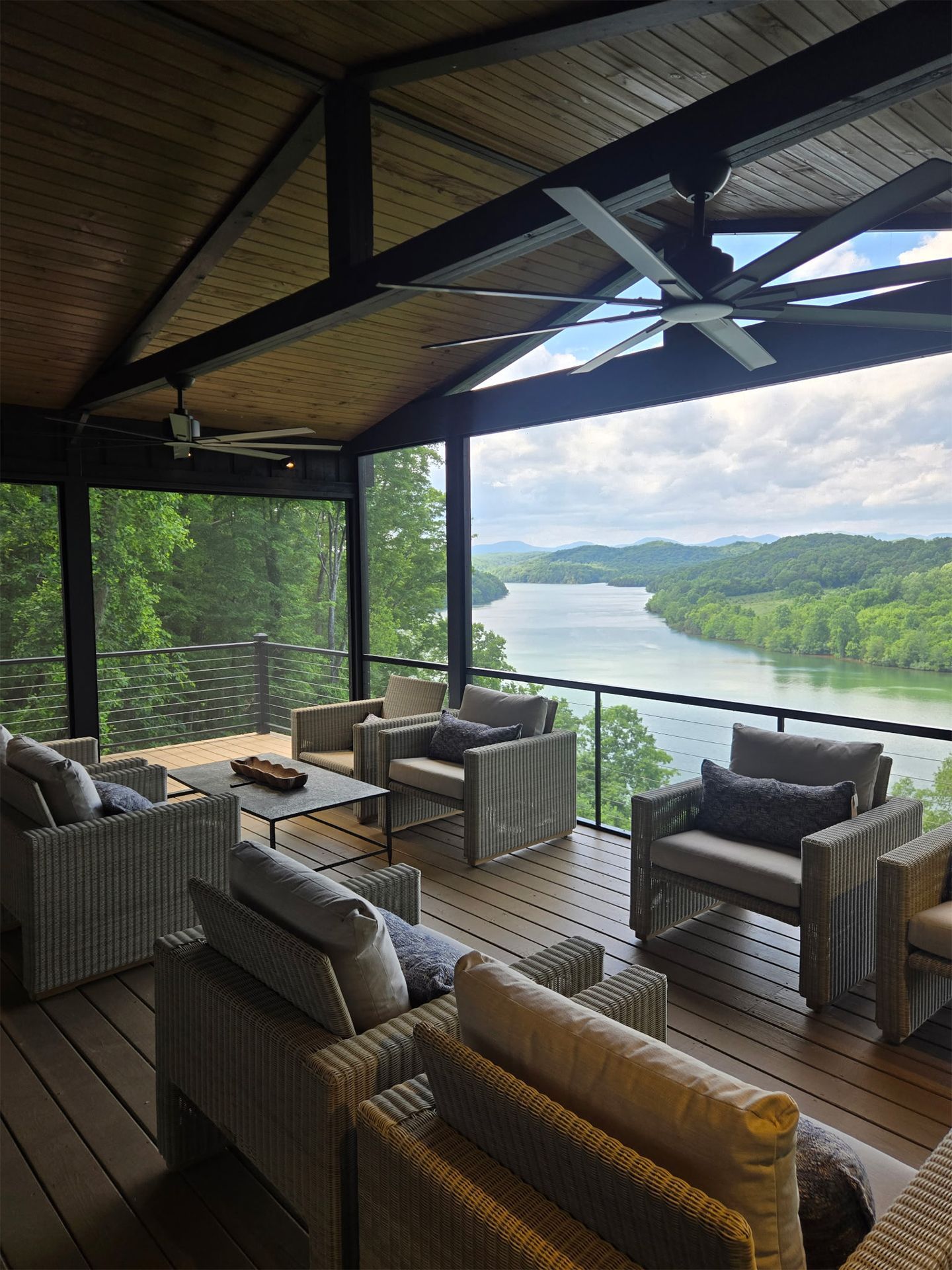Covered lakeside deck with wicker seating, ceiling fan, and panoramic water and hillside view