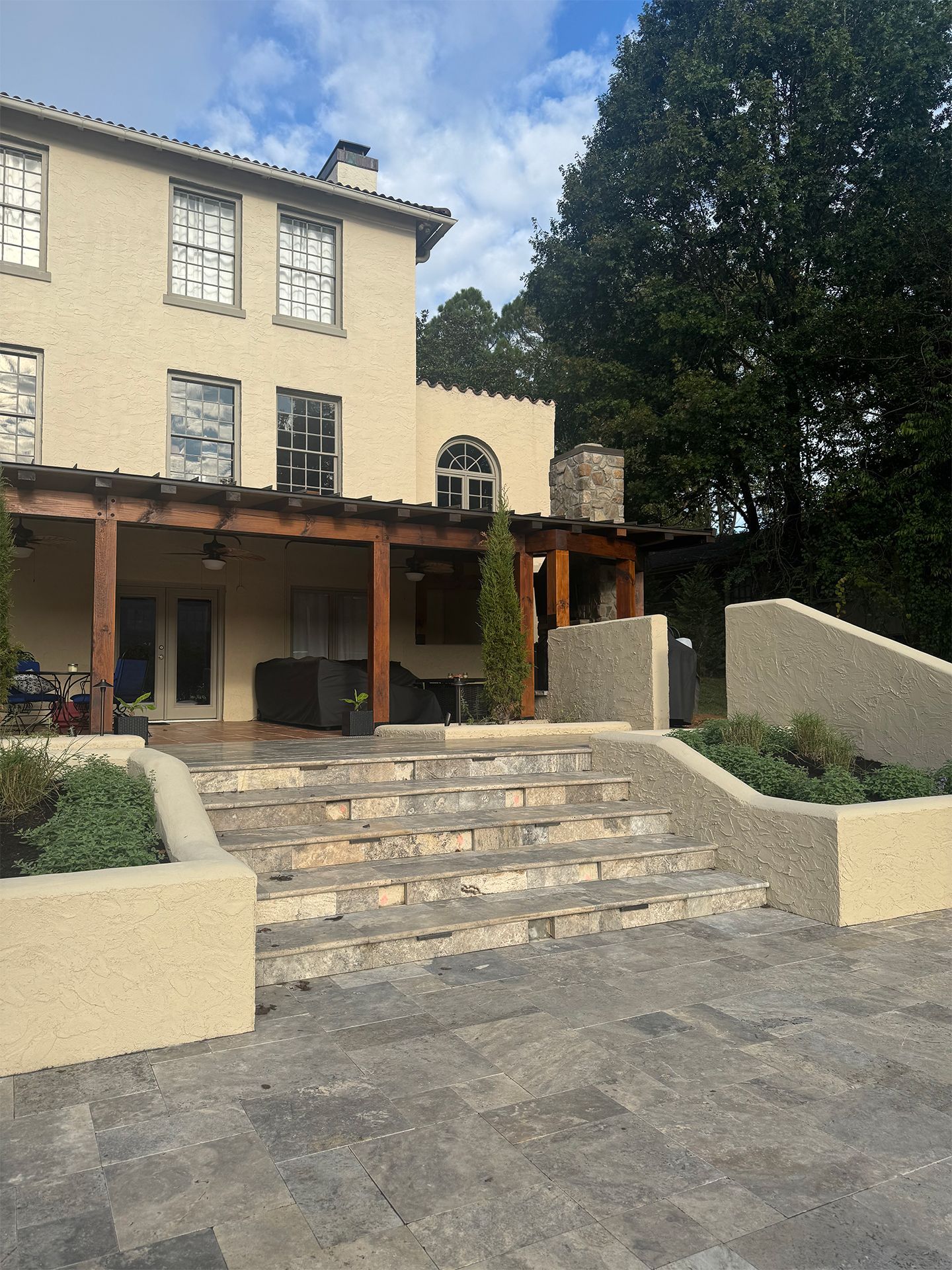 Stone steps lead to a beige building with a wooden porch and large tree beside it.
